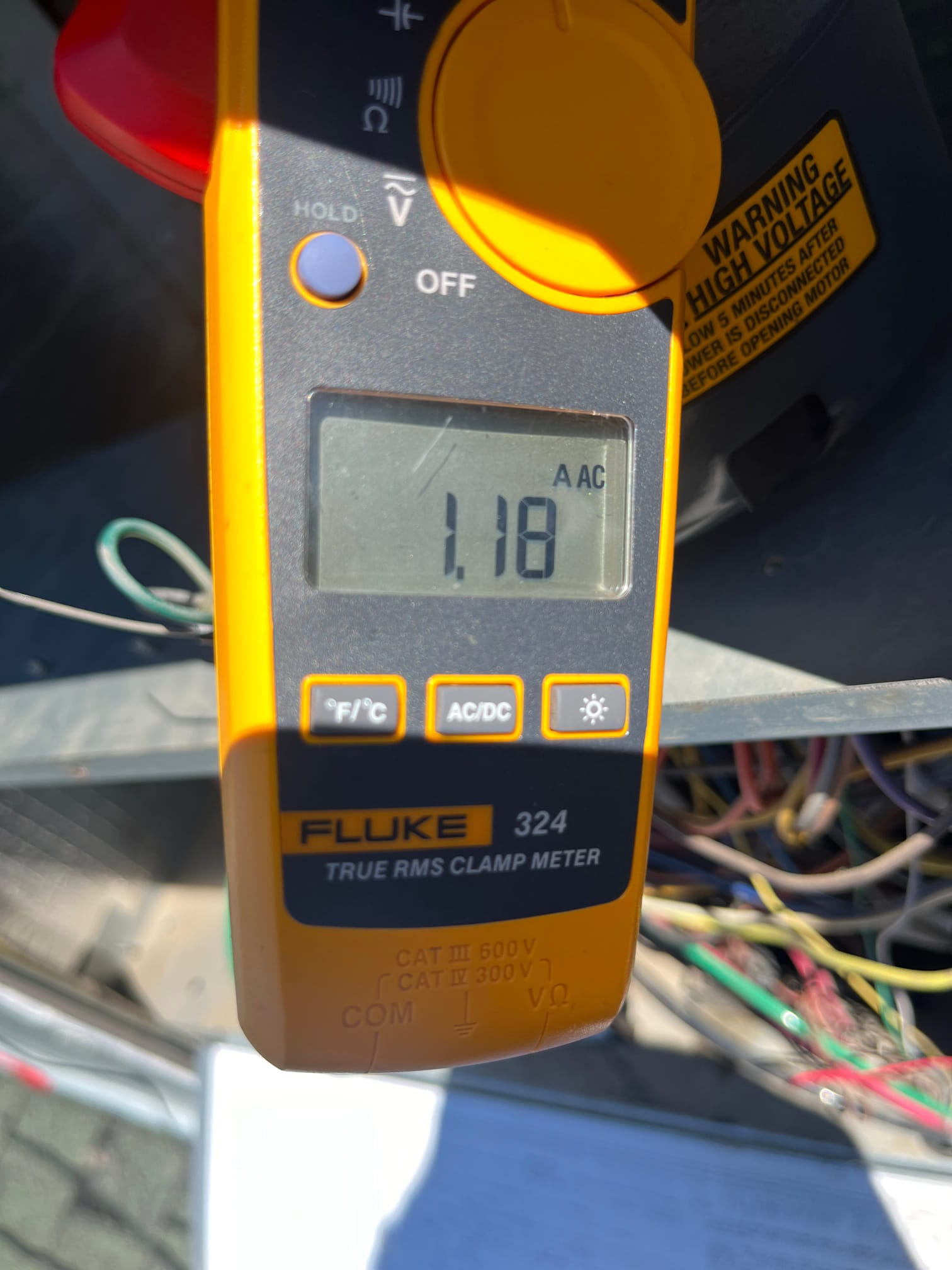 Clamp meter displays 1.18 A AC current while measuring a conductor inside the air conditioning equipment cabinet.