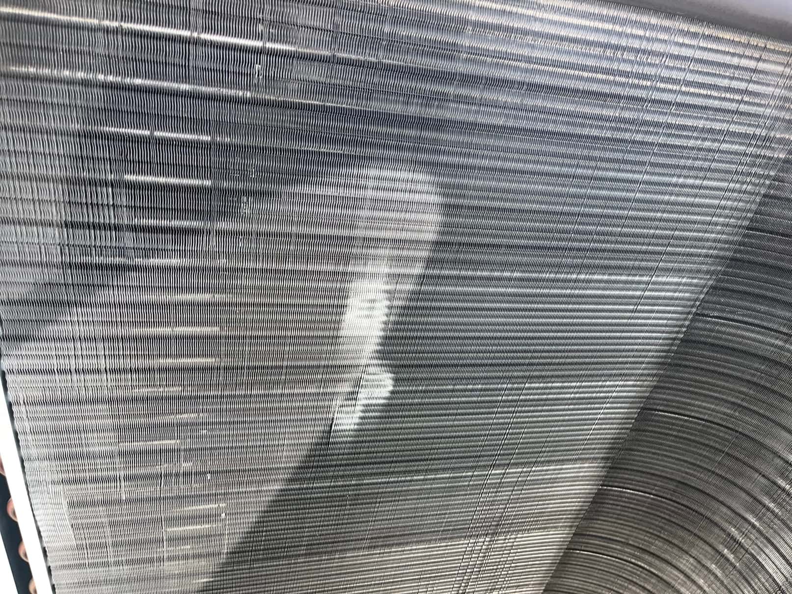 Close-up of an evaporator coil surface showing clean, straight fins with a small brushed area from recent cleaning.
