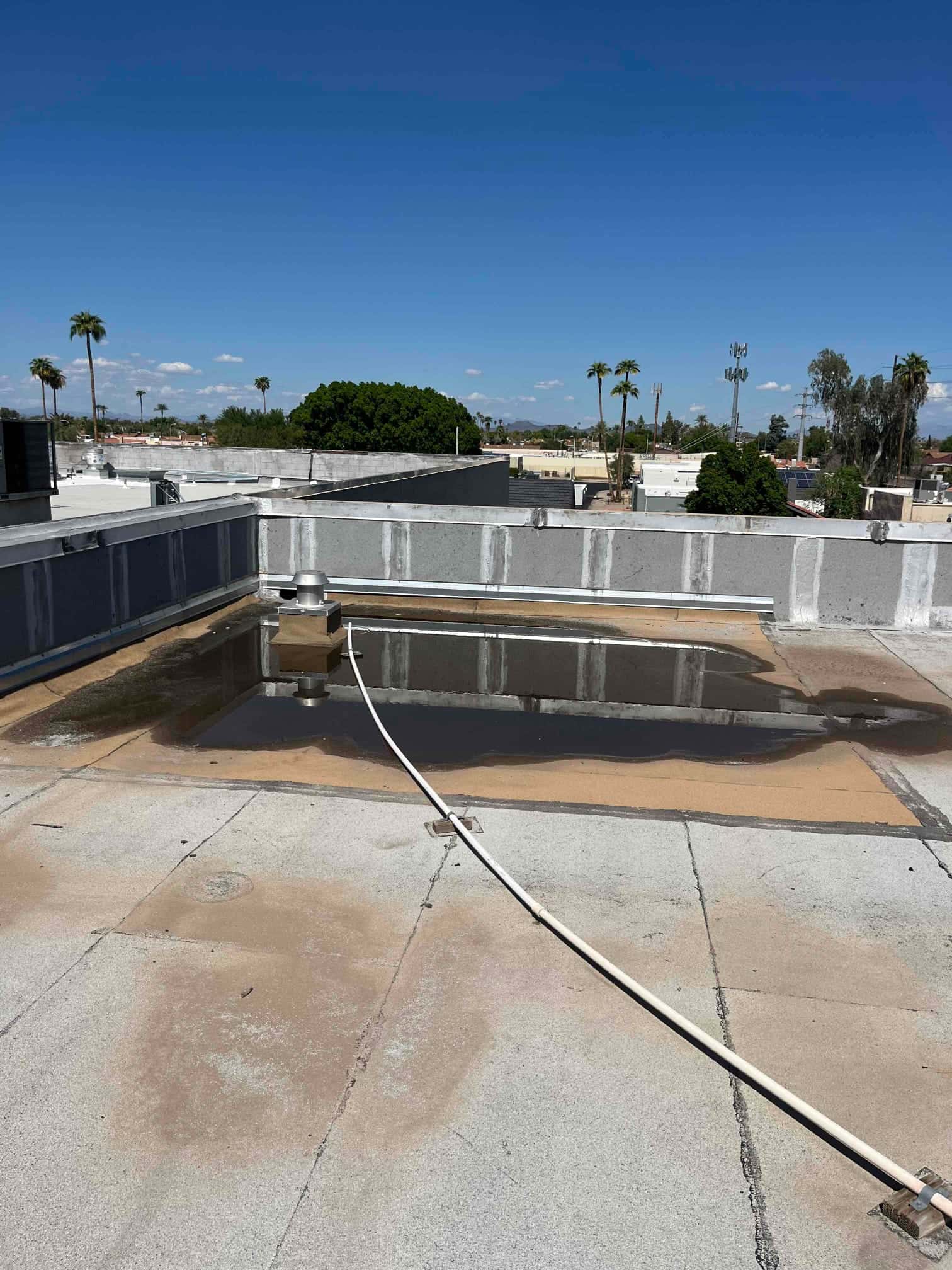 Commercial rooftop shows standing water near a vent and conduit, with surrounding HVAC curbs and parapet walls visible.
