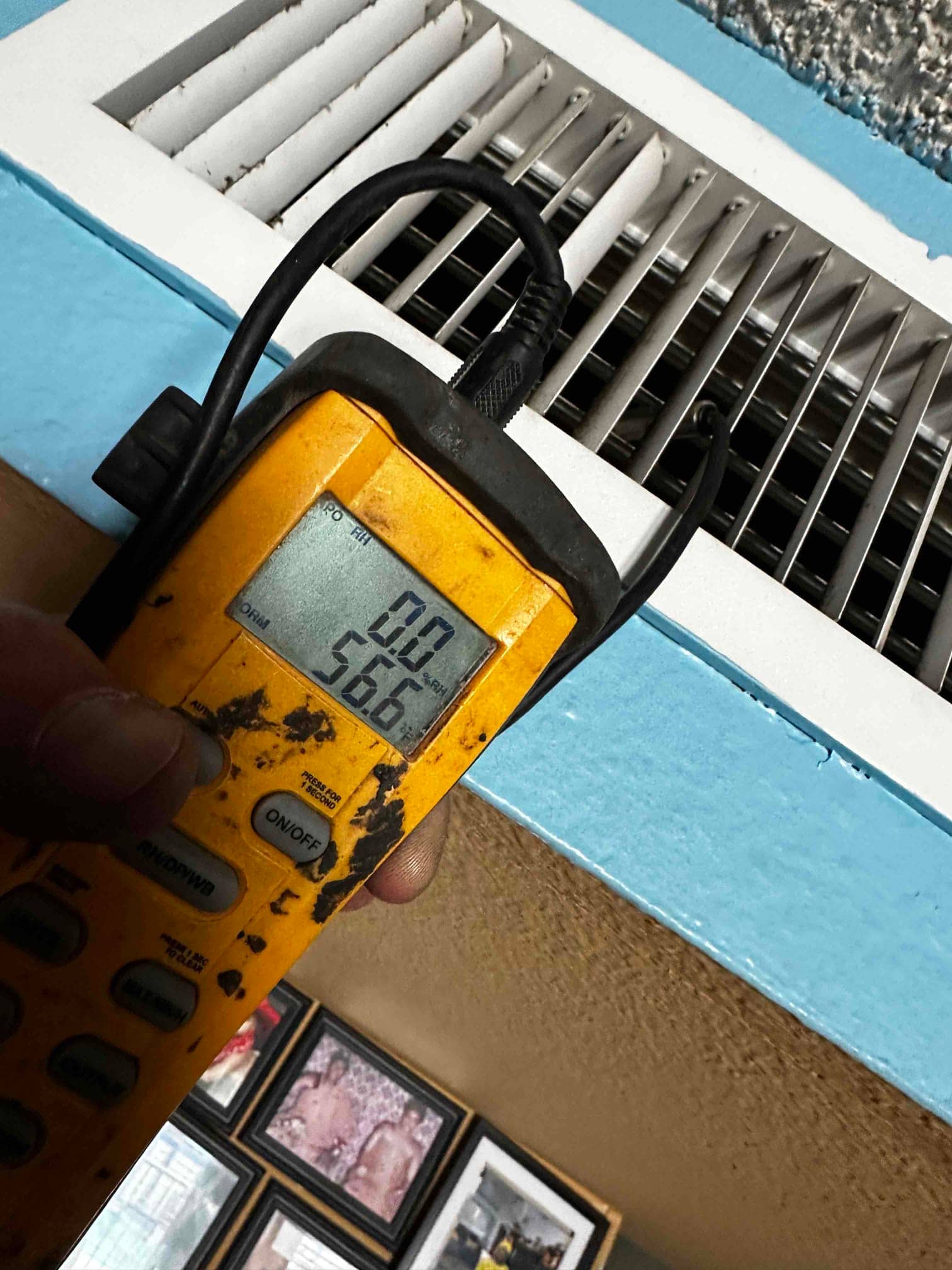 Digital thermometer held at a ceiling supply register shows 56.6 degrees Fahrenheit, documenting cooled supply air temperature.