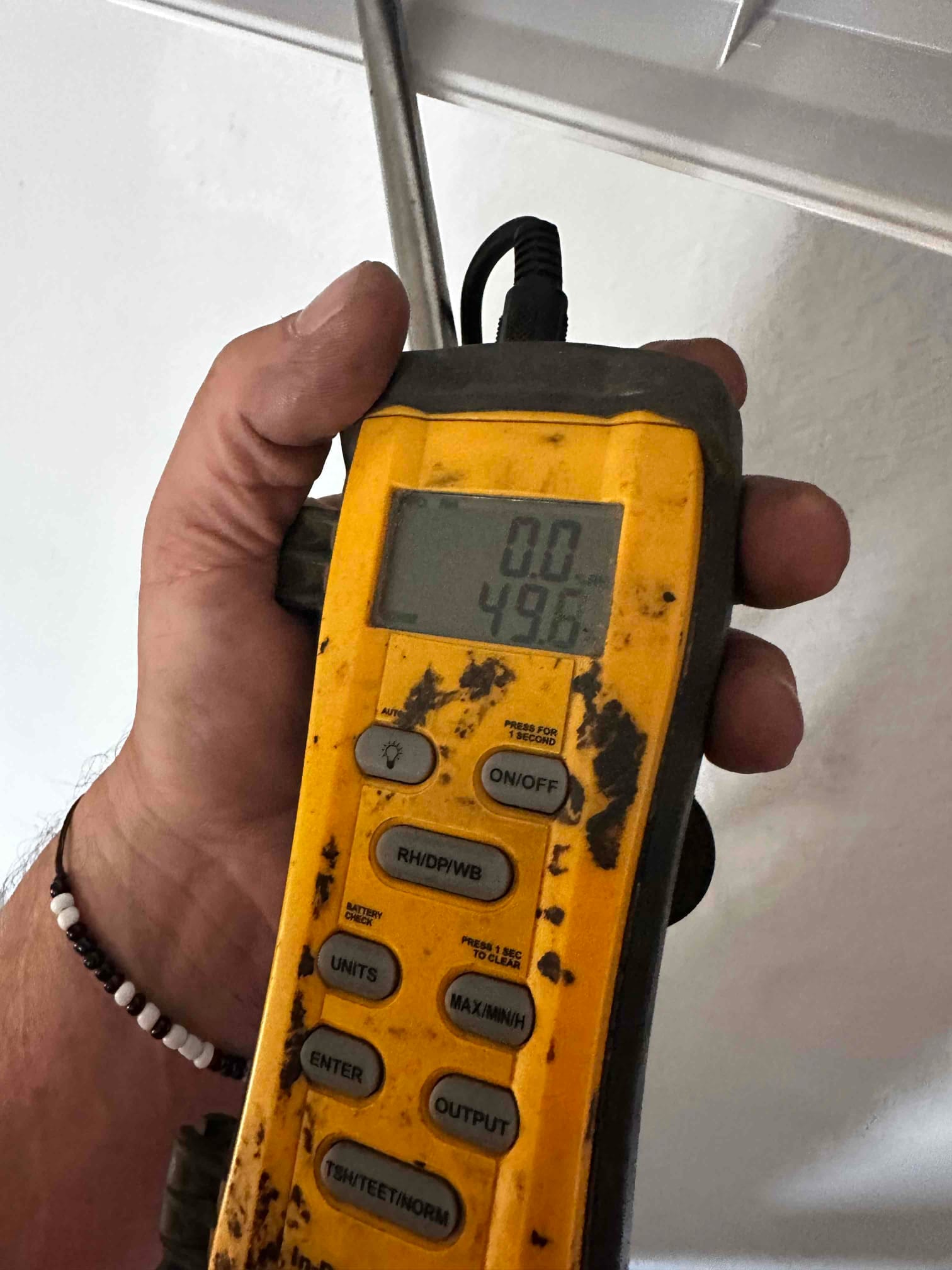 Digital thermometer probe inserted near a vent, display reading 49.6 degrees Fahrenheit during supply air temperature check.