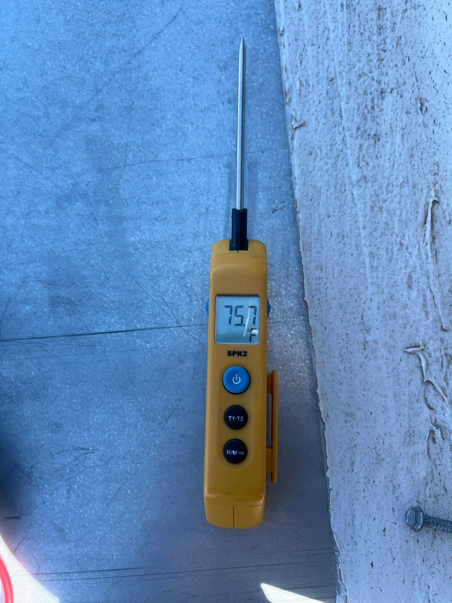 Digital thermometer with probe inserted reads 75.7 °F on the display during air conditioning service.