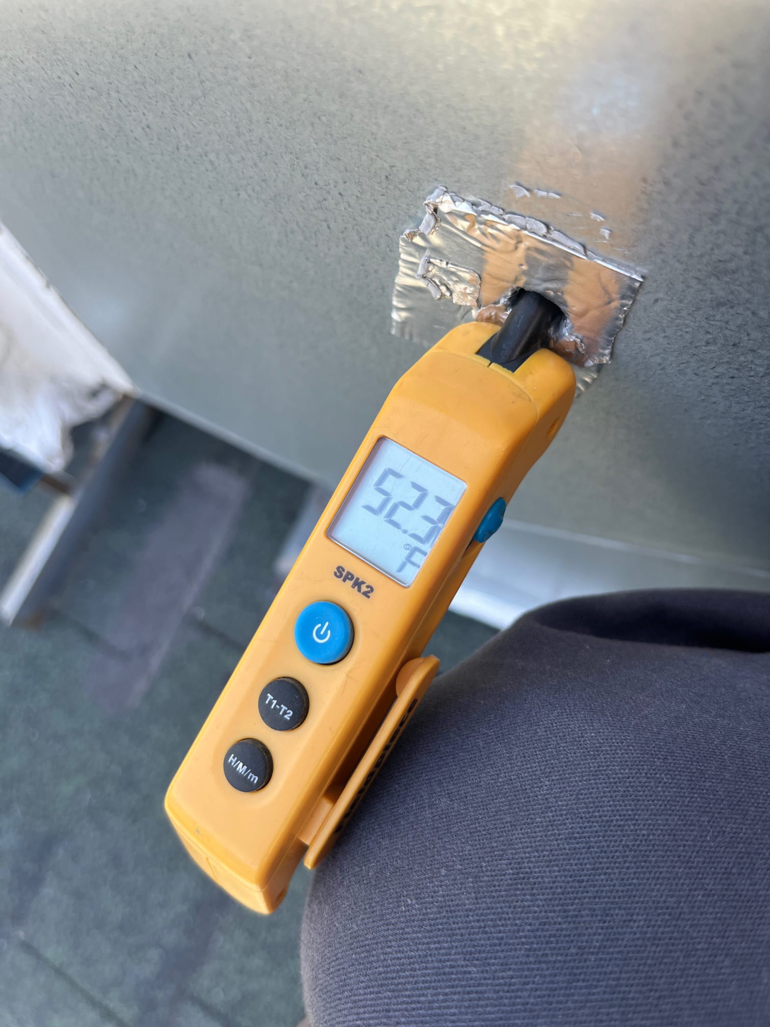 Digital thermometer shows 52.3 °F with the probe inserted into a taped opening on the metal duct surface.