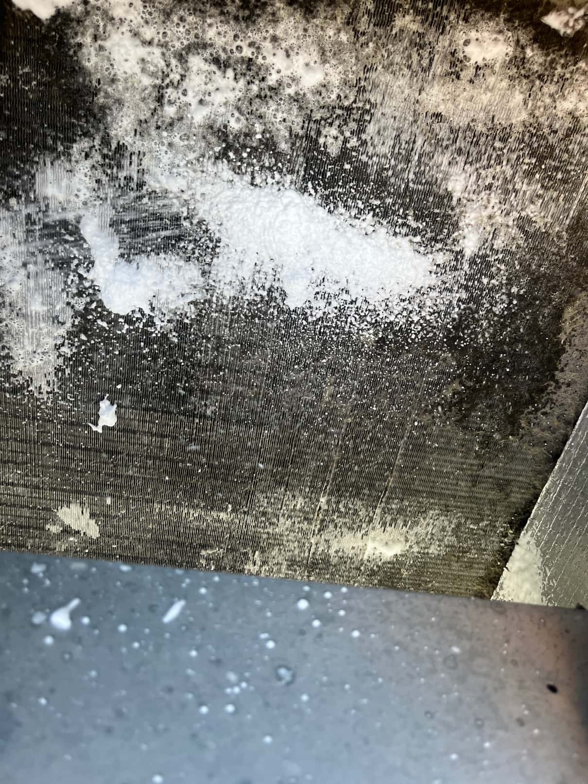 Dirty evaporator coil fins with cleaner foam applied, showing accumulated dust and residue before thorough cleaning.