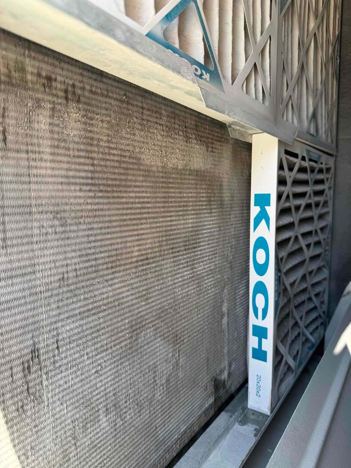 Dusty evaporator coil and pleated air filters inside an air handler, showing accumulated debris on the coil surface.