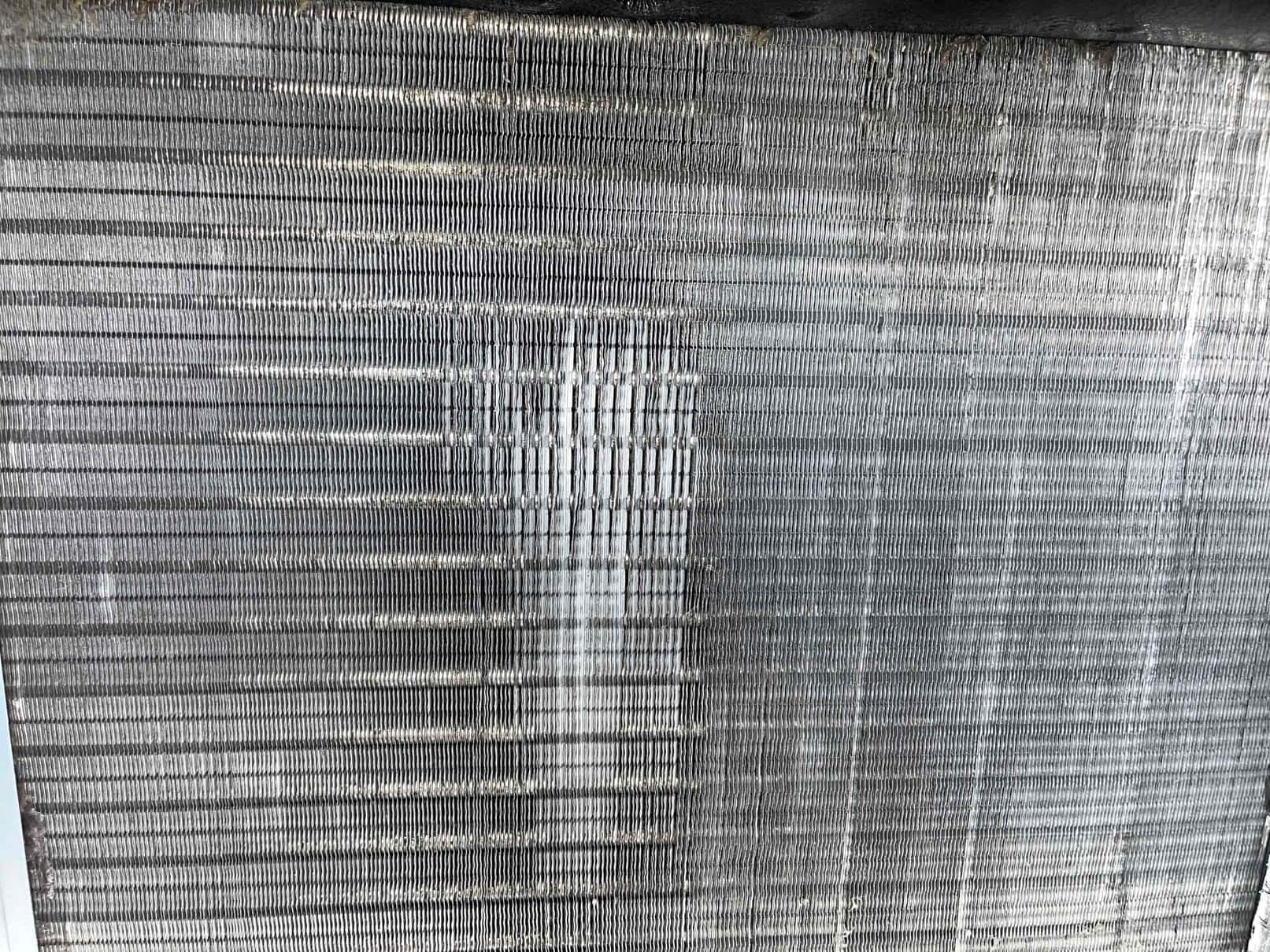 Evaporator coil fins after cleaning, showing uniform fin structure with remaining light surface oxidation and streaking.