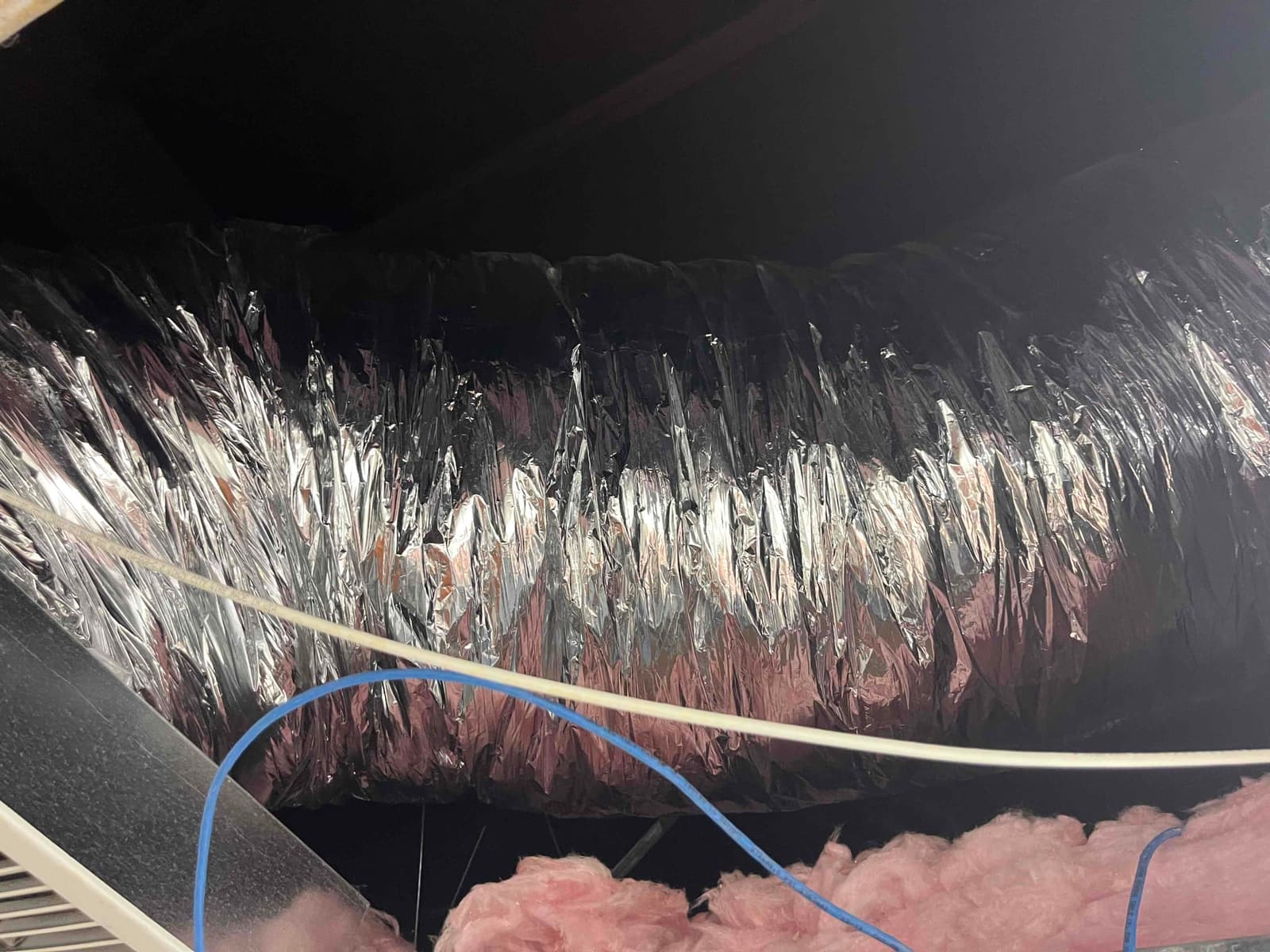 Flex insulated duct with reflective jacket runs above ceiling grid, with exposed pink fiberglass insulation and low-voltage wires visible.