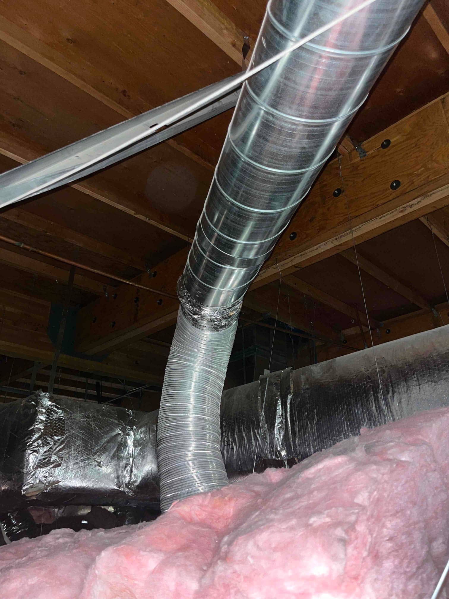Flexible duct transitions to a rigid metal duct above pink fiberglass insulation in a ceiling framing space.