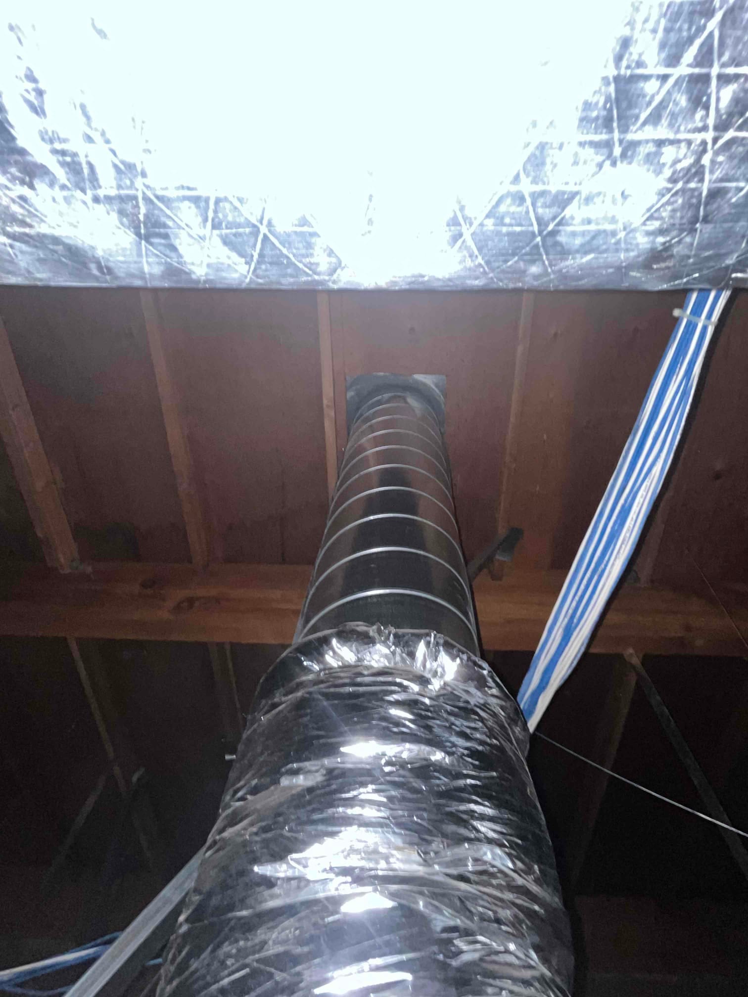Flexible insulated duct run suspended from the ceiling joists, showing spiral reinforcement and foil-faced insulation wrap.