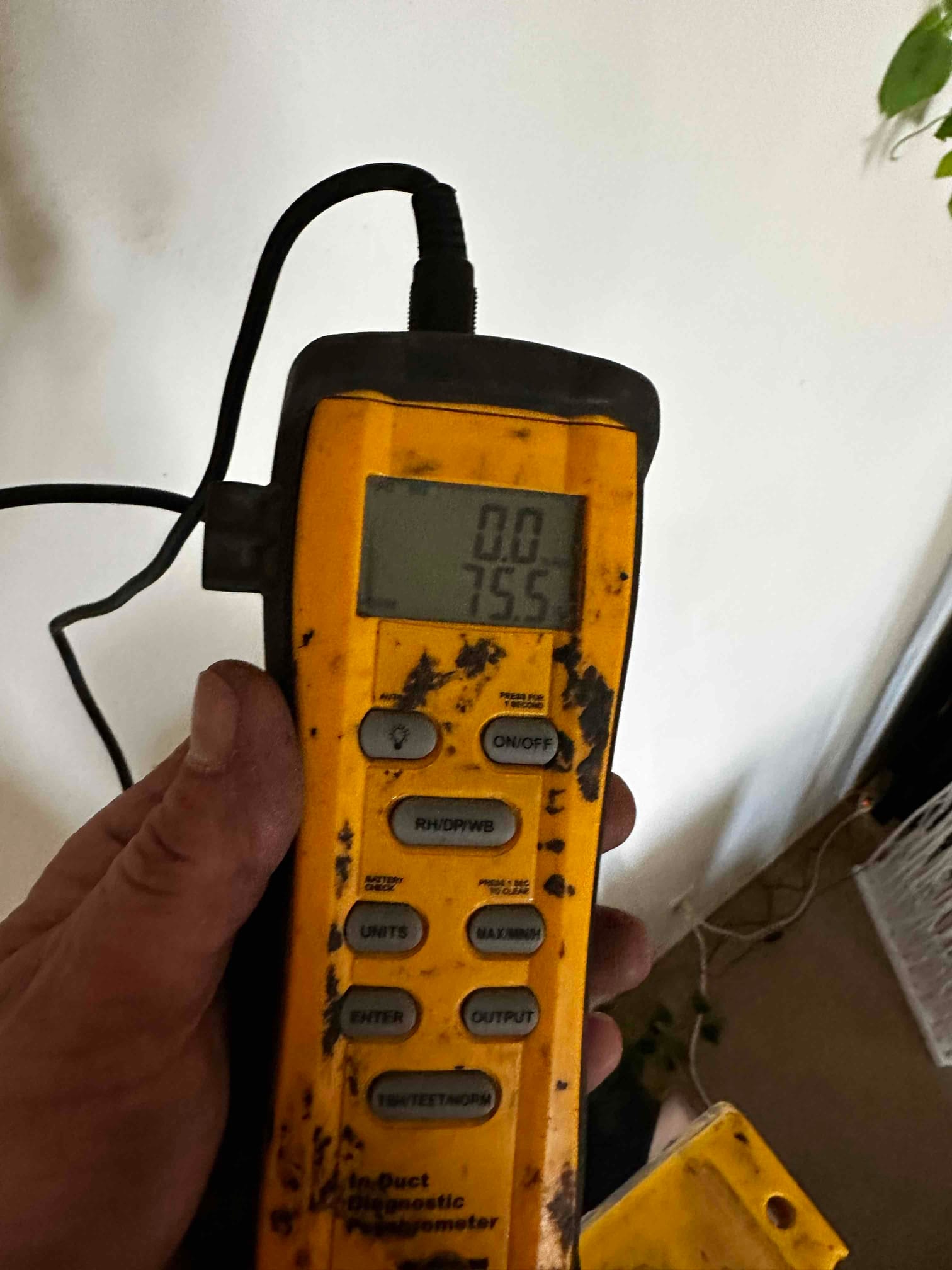 Handheld digital thermometer displays 75.5 degrees Fahrenheit while measuring indoor air temperature during commissioning.