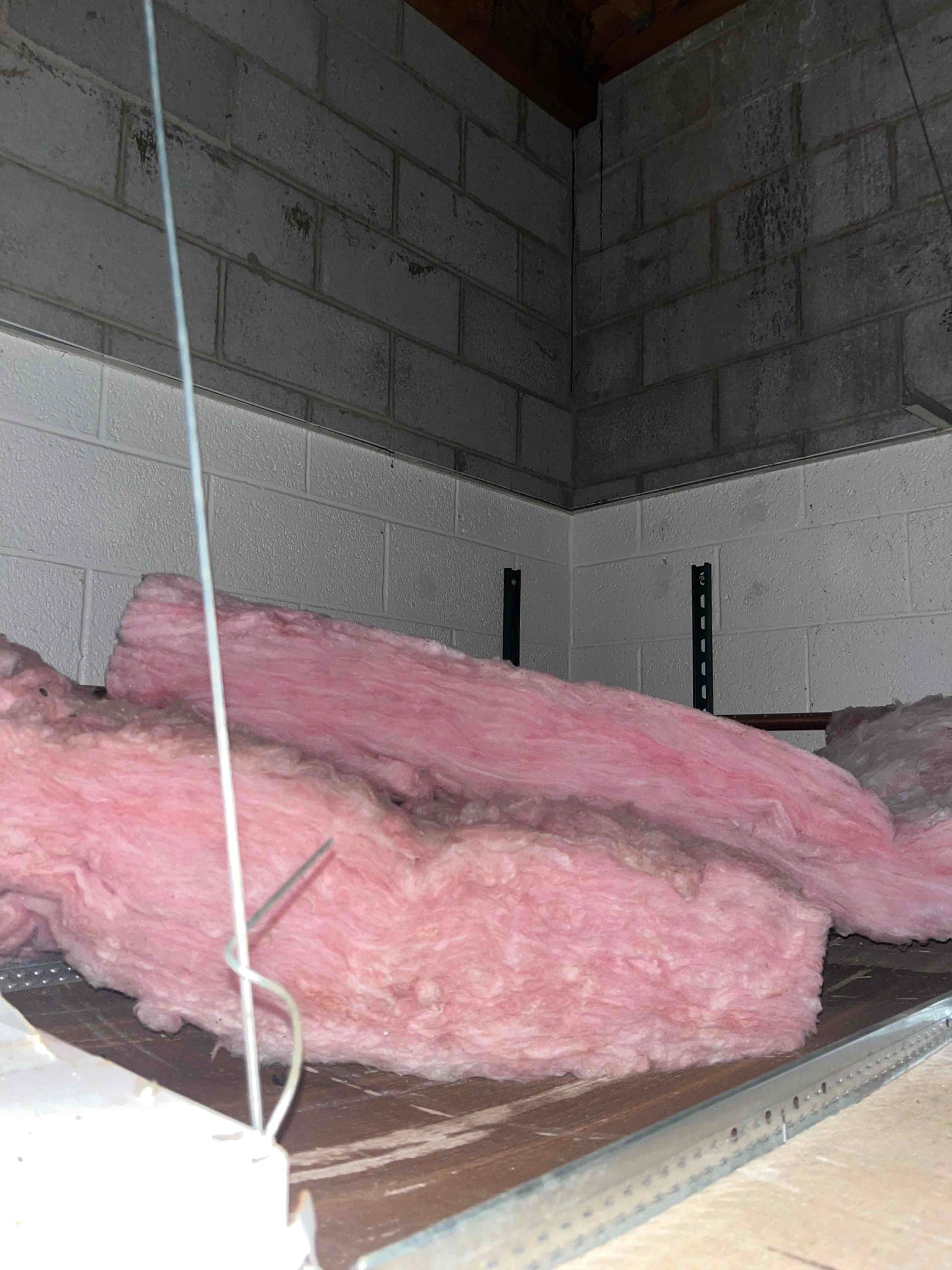 Loose pink fiberglass insulation laid on a storage platform in a mechanical space with concrete block walls.