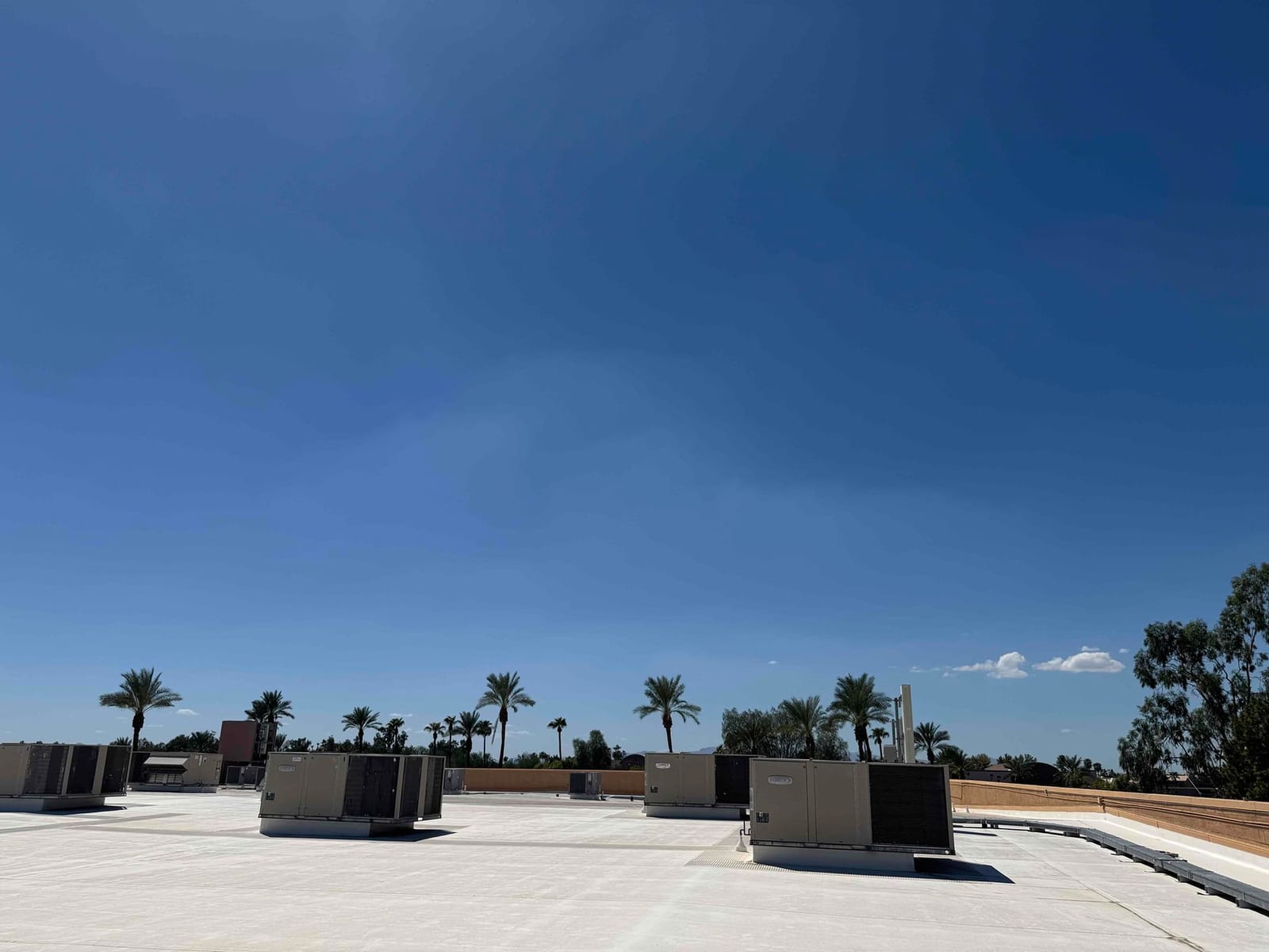 Multiple rooftop air conditioning units installed on a commercial building, shown under clear sky with visible ductwork and curb mounts.
