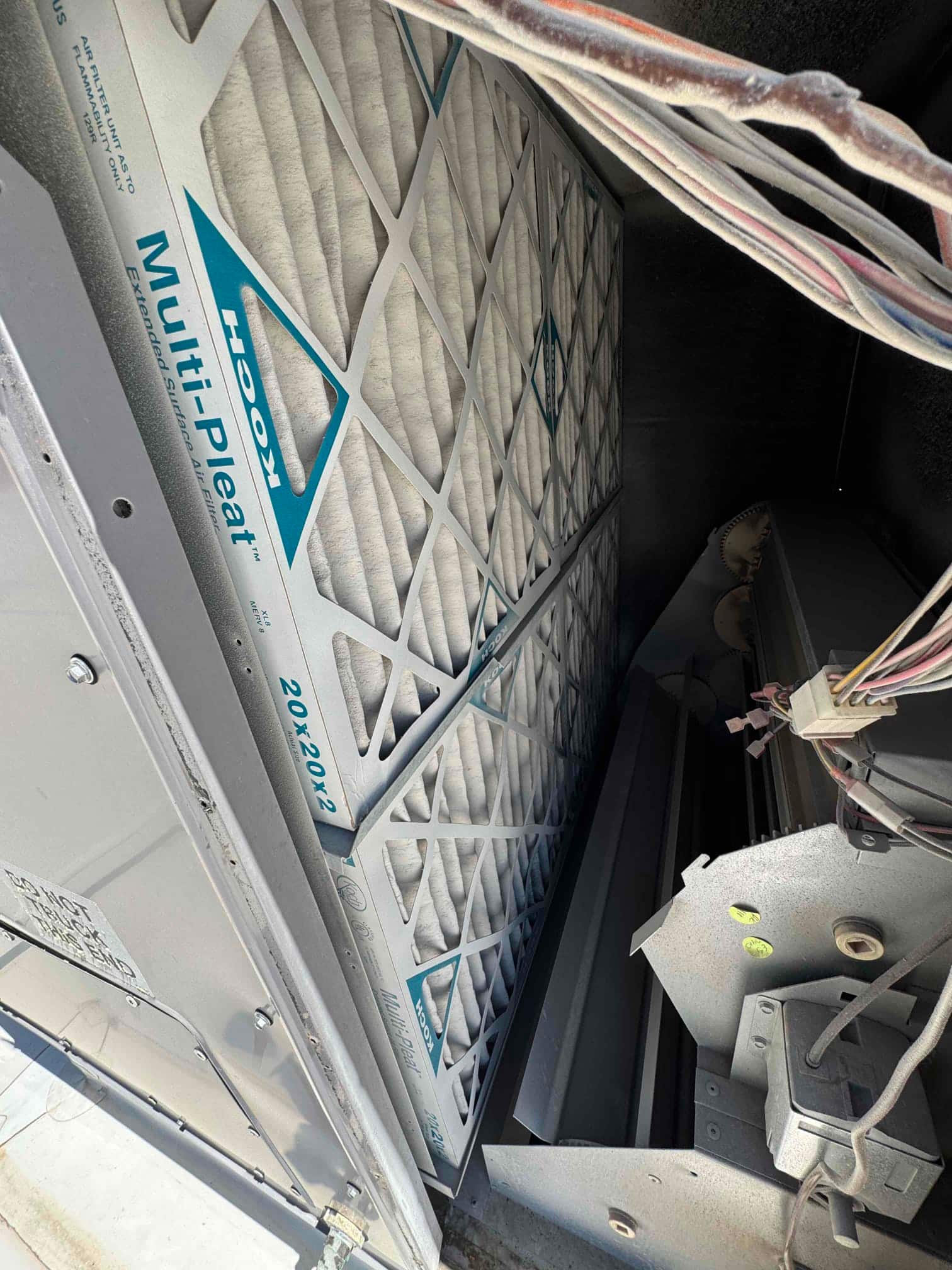 New pleated air filters installed inside the commercial air handler, with nearby control wiring and blower housing visible.