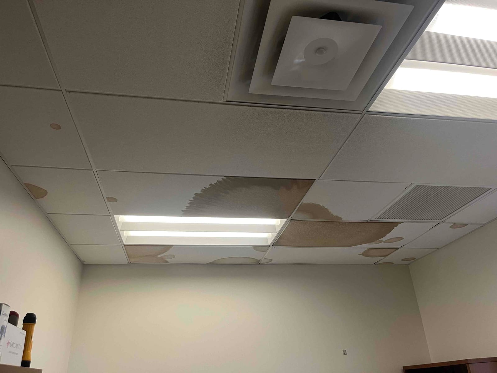 Office ceiling shows multiple water-stained acoustic tiles near diffuser and return grille, indicating moisture intrusion from HVAC system or nearby piping.