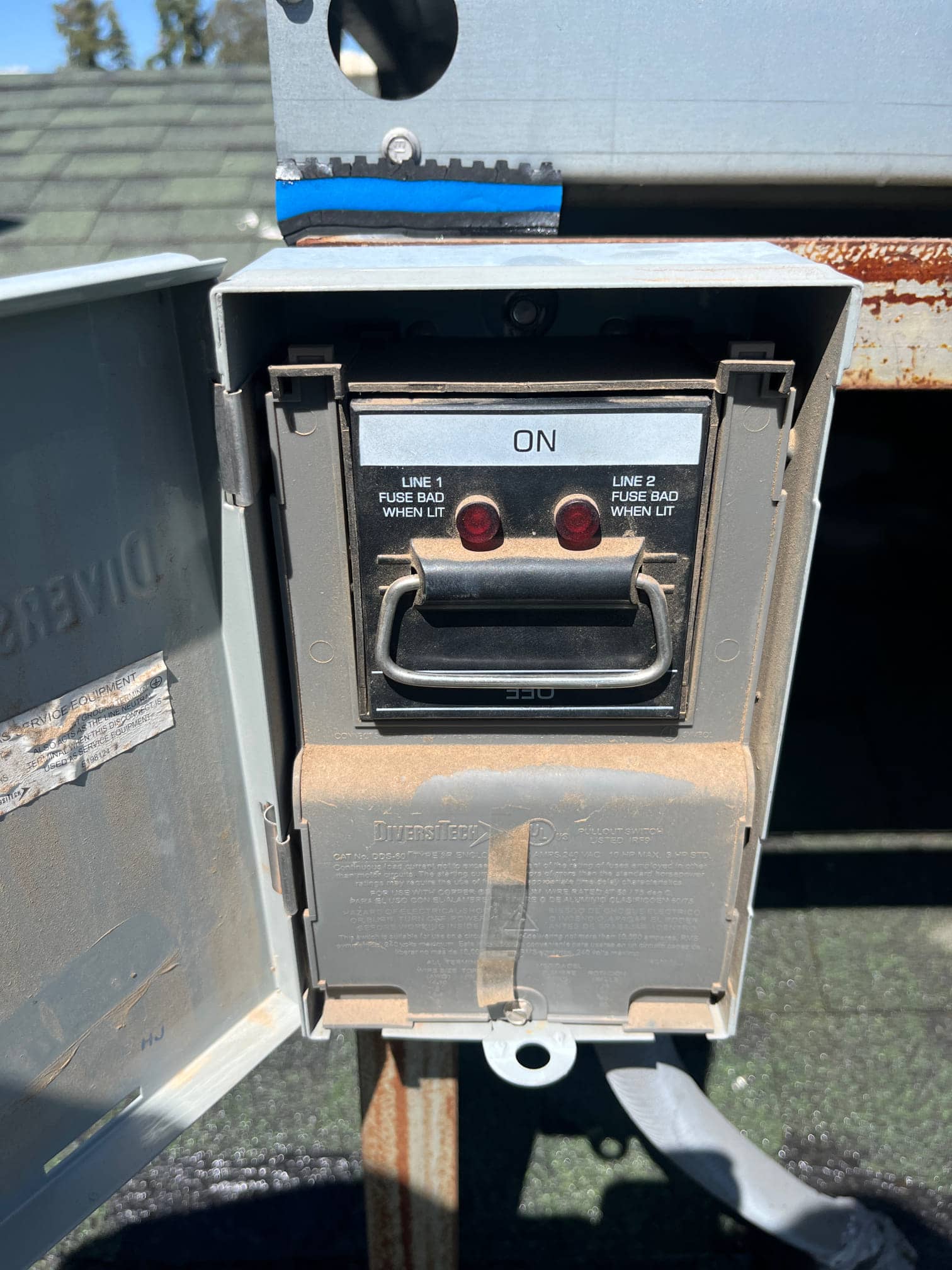 Outdoor AC disconnect with pull handle in ON position, showing two indicator windows labeled for line fuses when lit.