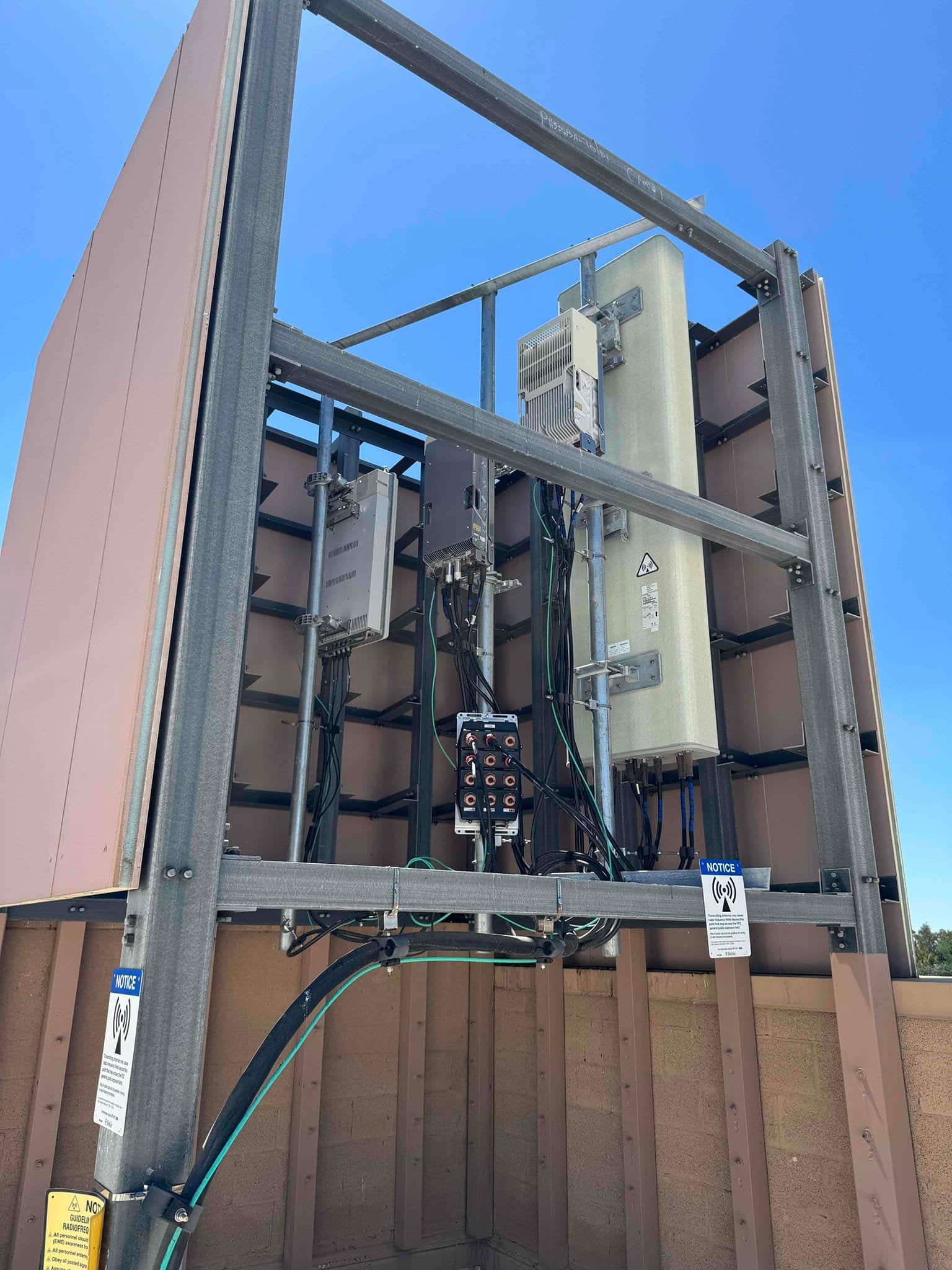 Outdoor electrical service rack with conduit and control box mounted on a rooftop enclosure, showing wiring and protective panels.