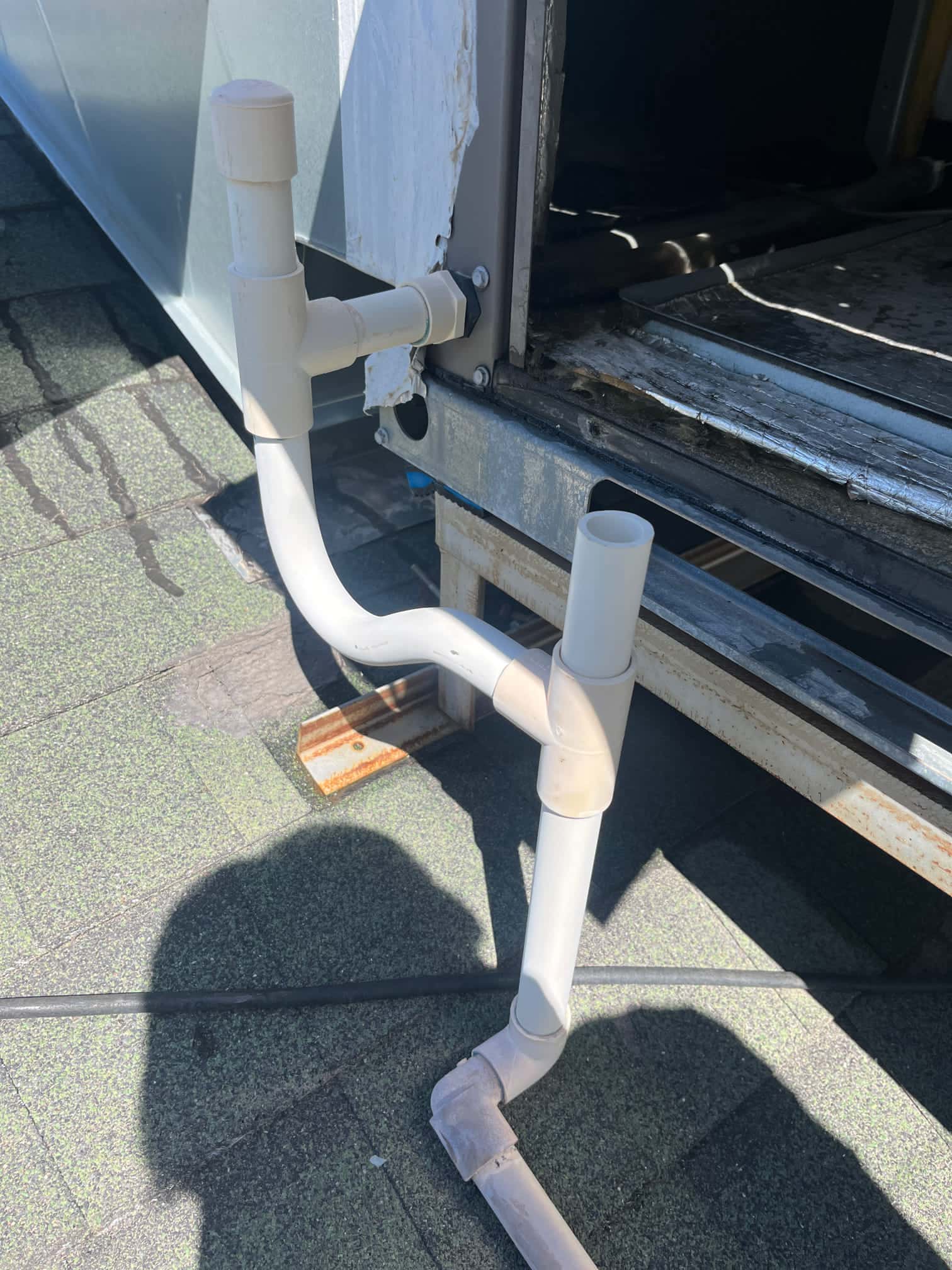 PVC condensate drain piping at an air handler cabinet on a rooftop, showing multiple tees and elbows with open standpipes.