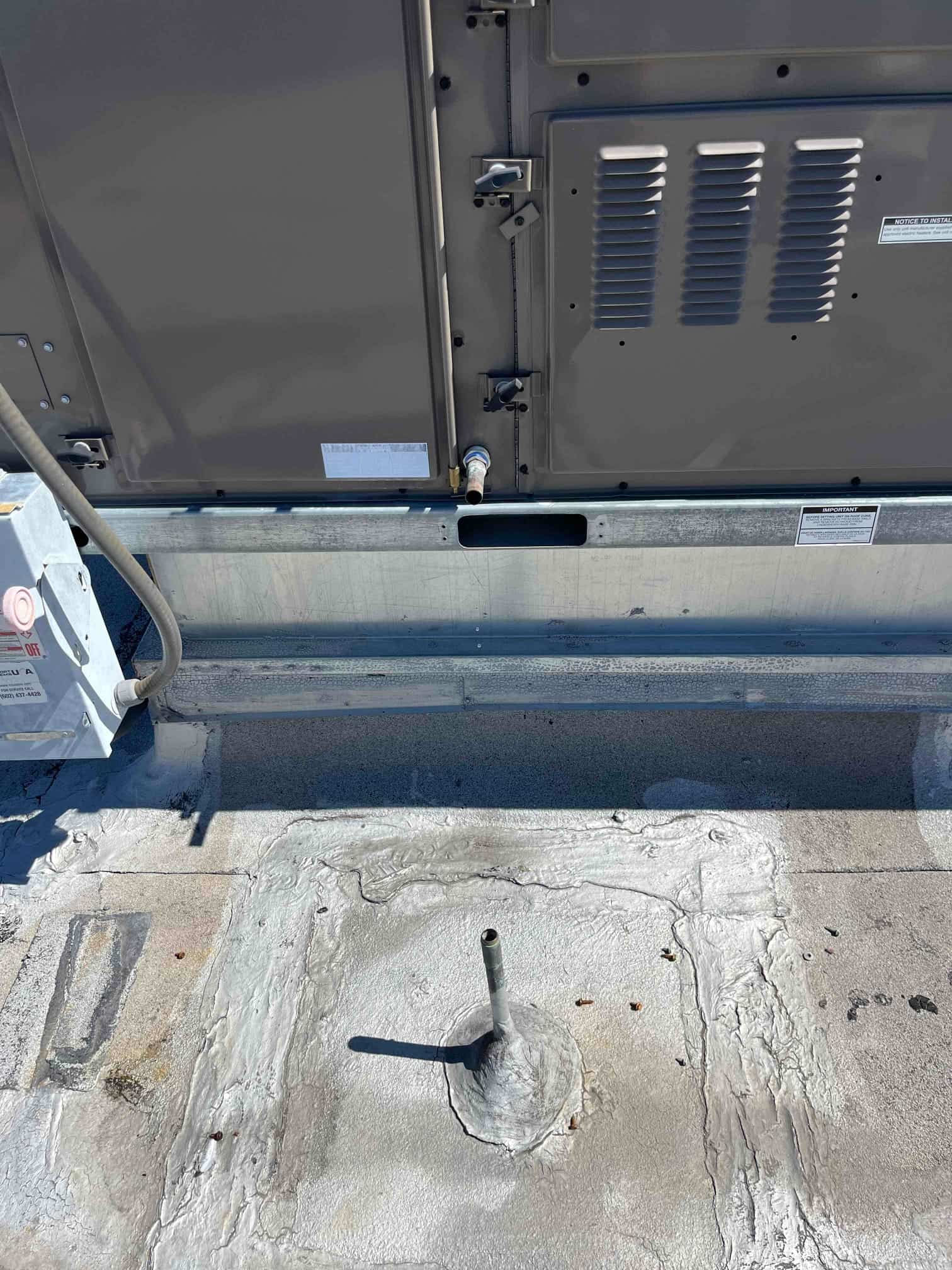 Rooftop commercial HVAC unit exterior with service panel and condensate drain line above a sealed roof curb.