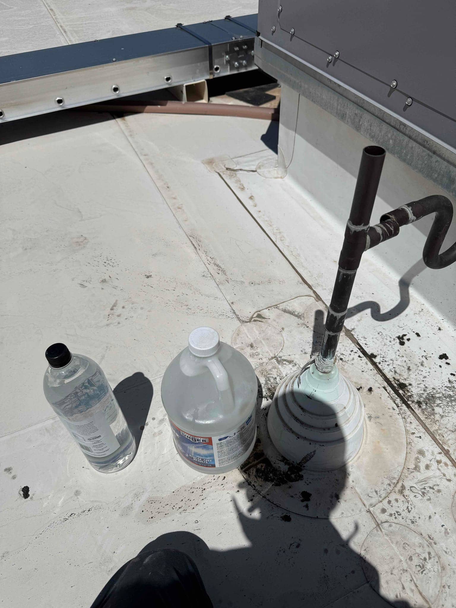 Rooftop condensate drain cleanout with plumbing vent and cleaning solution containers placed beside the drain on the roof.