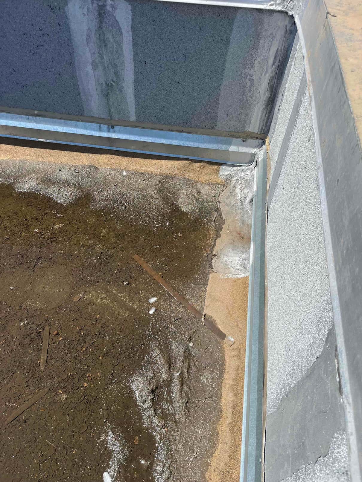 Rooftop equipment curb interior shows pooled water, rust, and deteriorated sealant along the metal curb joint.