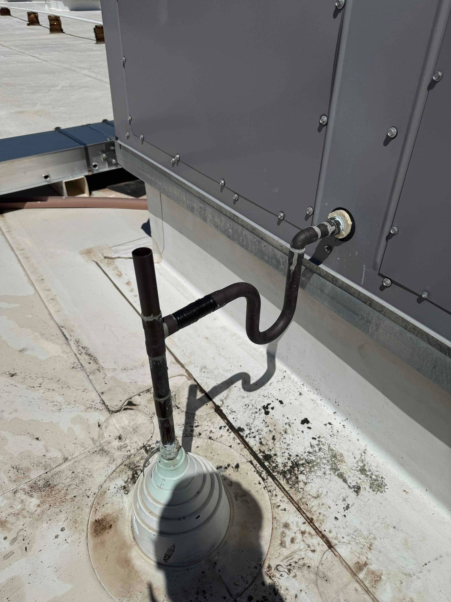 Rooftop HVAC unit condensate drain and trap assembly installed, showing PVC riser, P-trap, and sealed wall penetration.