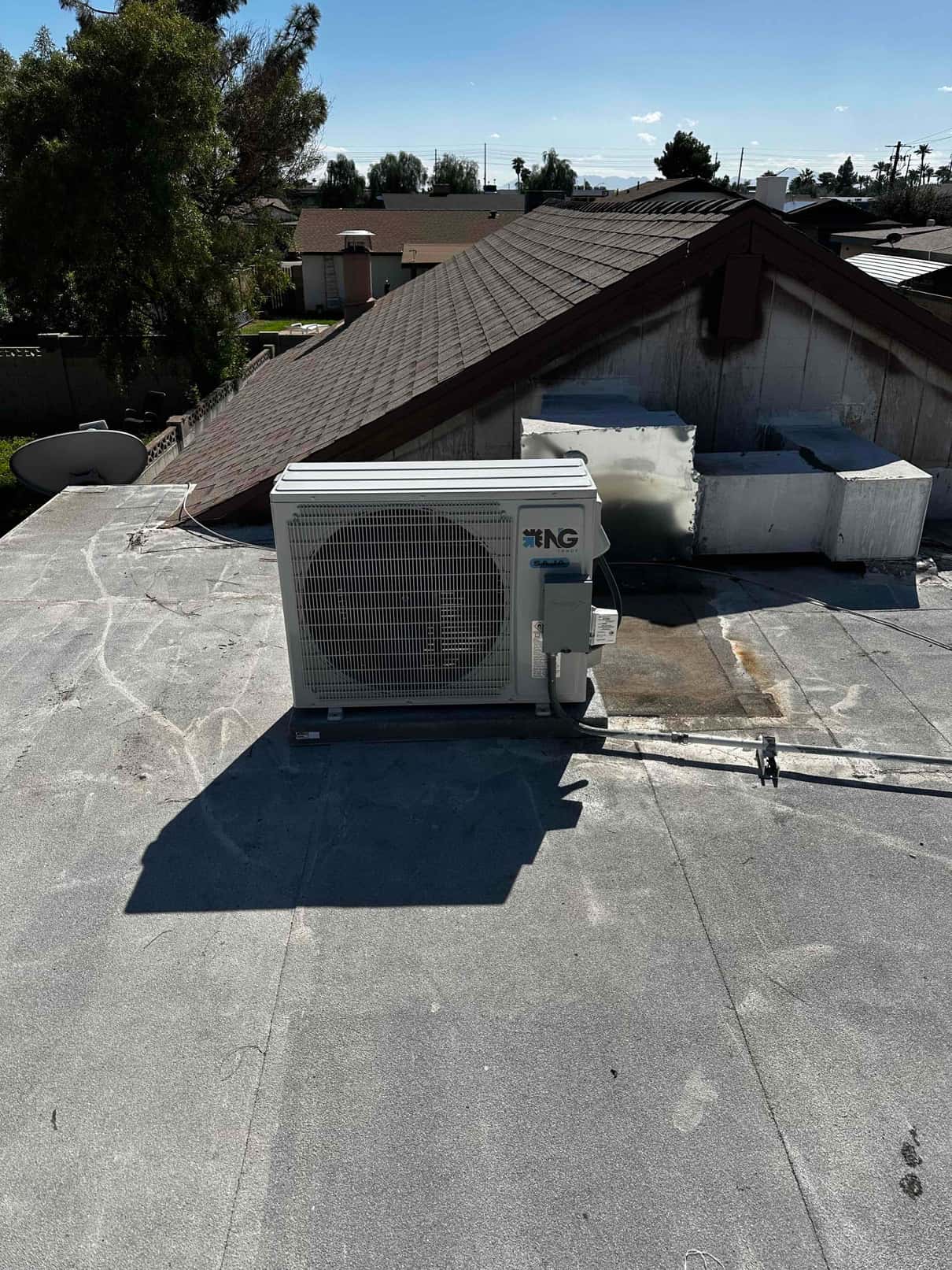 Rooftop mini-split condenser set on a level surface with armored line set and electrical whip routed to the unit.