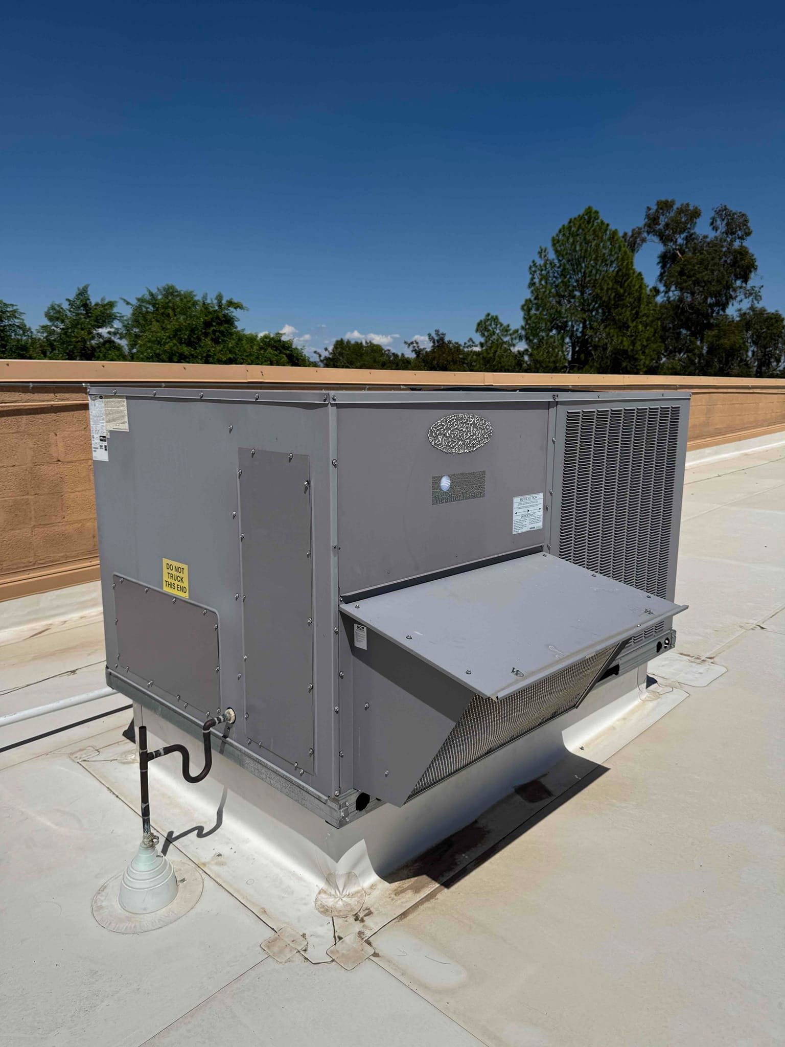 Rooftop packaged air conditioning unit on a commercial building, showing condenser section, service panel, condensate drain, and surrounding roof area.