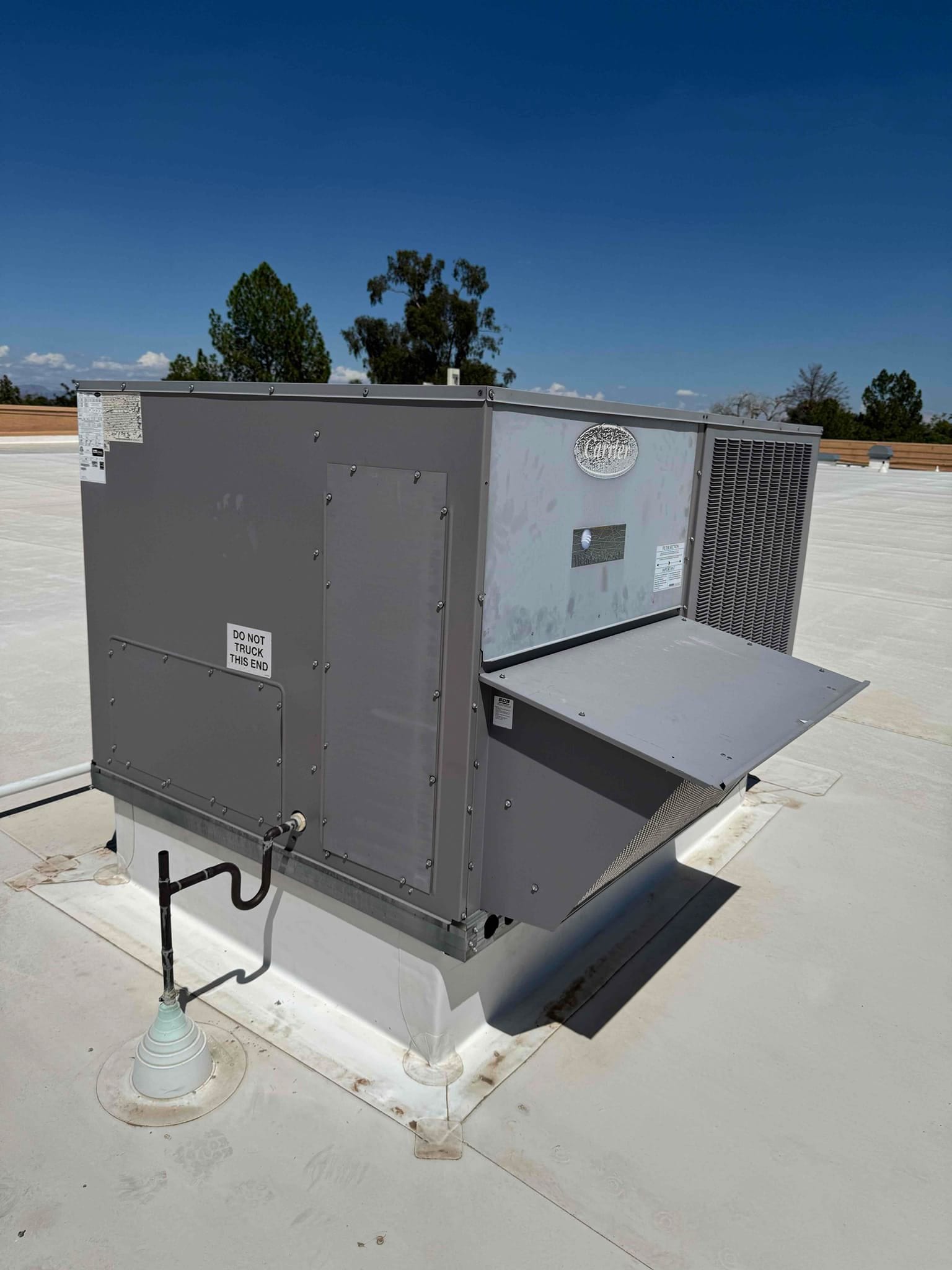 Rooftop packaged air conditioning unit on a flat commercial roof, access panel open to the filter or return section.