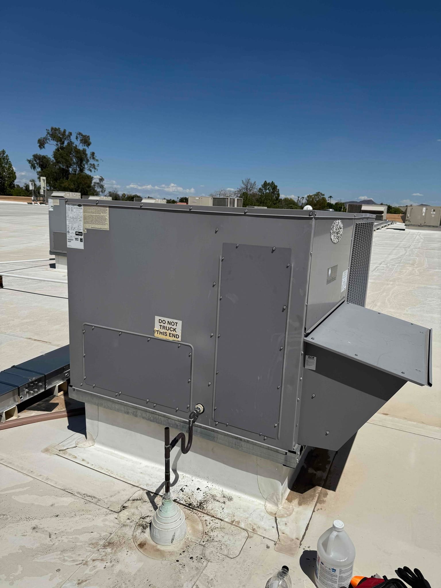 Rooftop packaged HVAC unit on a commercial building, access panels closed, condensate drain visible, and surrounding roof equipment nearby.
