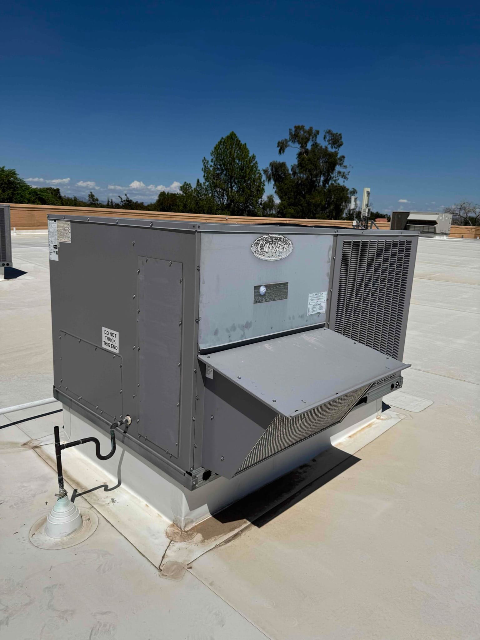 Rooftop packaged HVAC unit on a commercial building, showing condenser coil, service panels, and condensate drain on the curb.