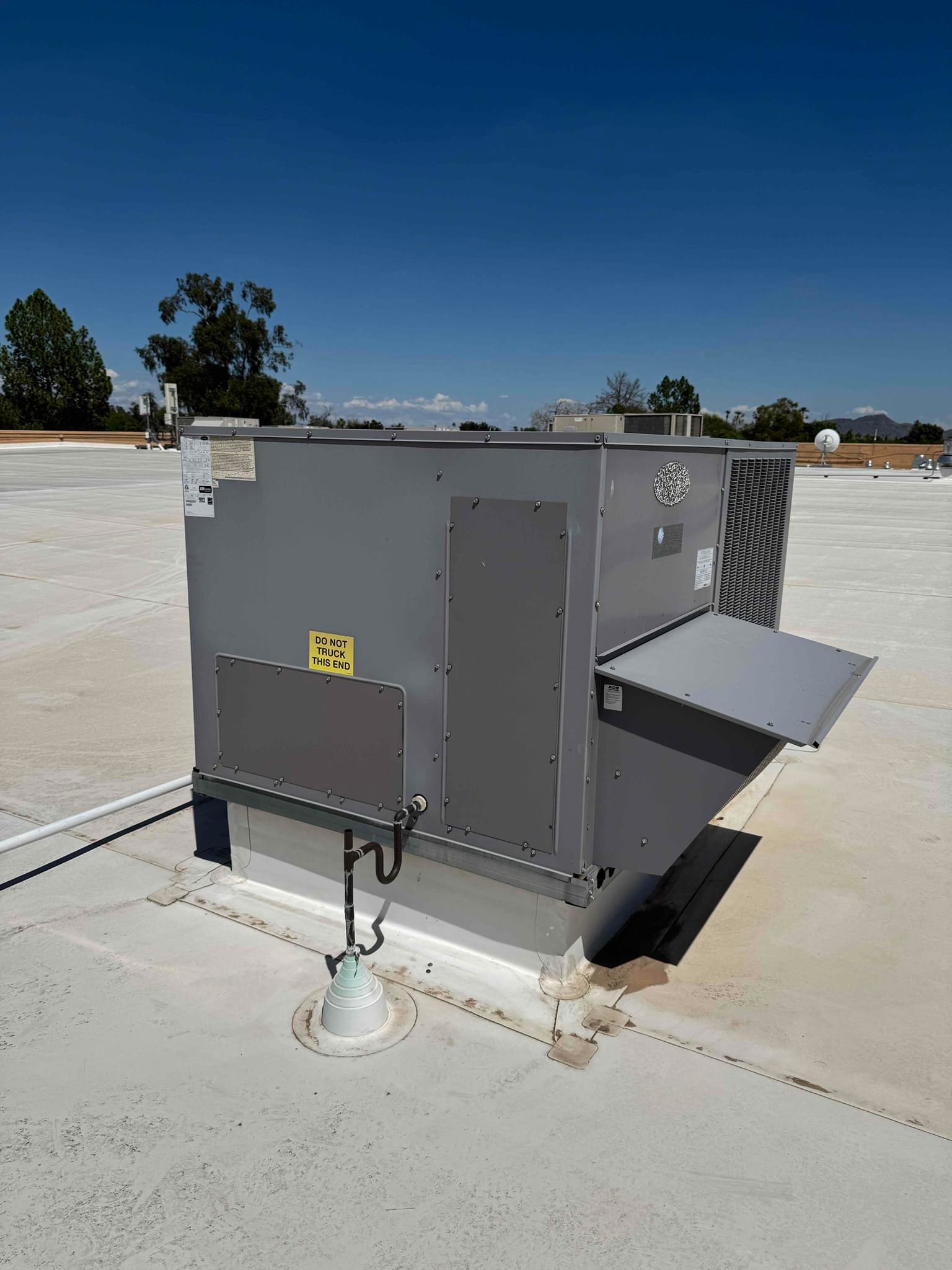 Rooftop packaged HVAC unit on a commercial building roof, access panel closed, with electrical conduit and disconnect visible.