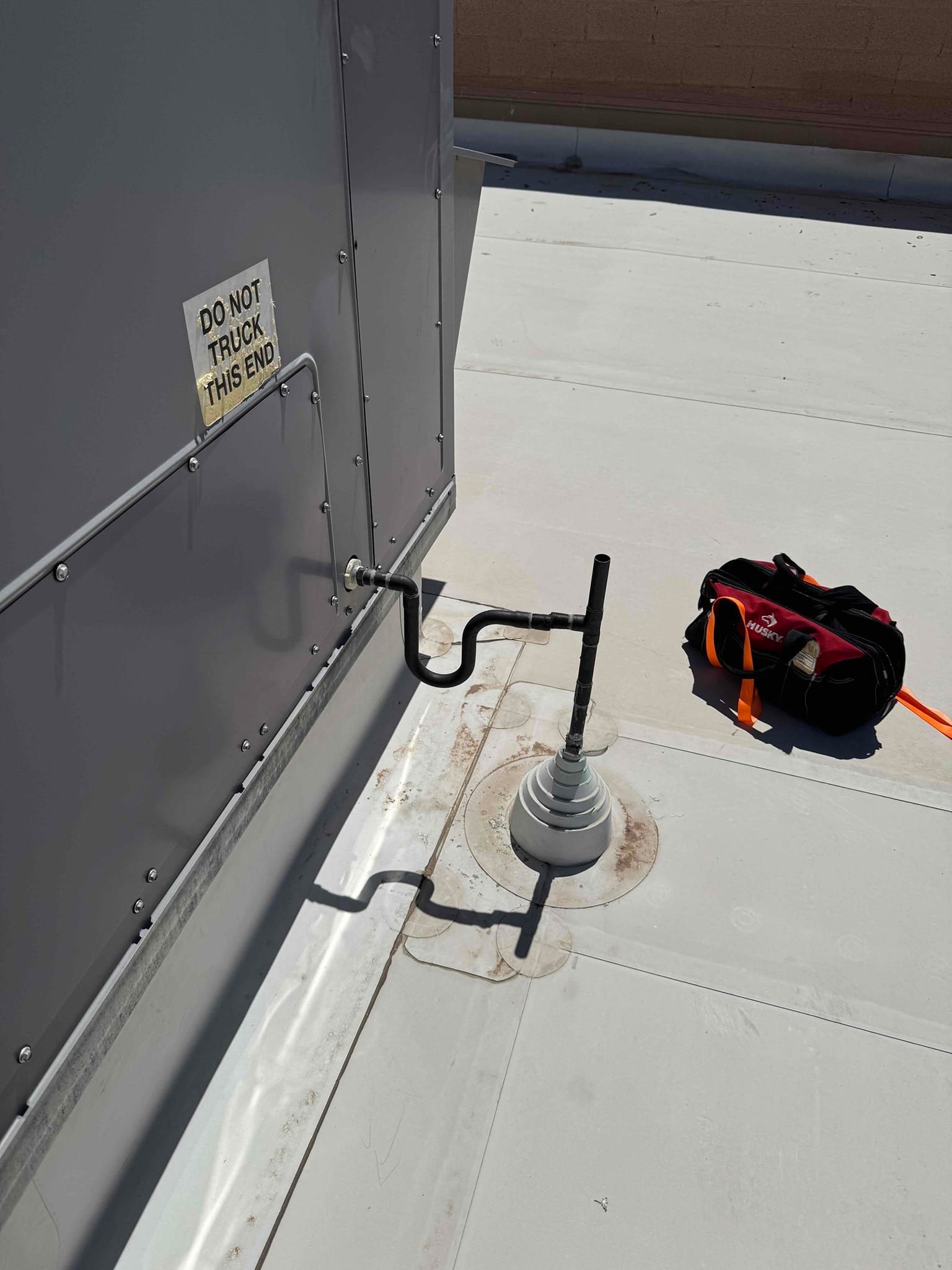 Rooftop packaged HVAC unit condensate drain piping with cleanout and roof penetration boot, showing secure supports and neat installation.