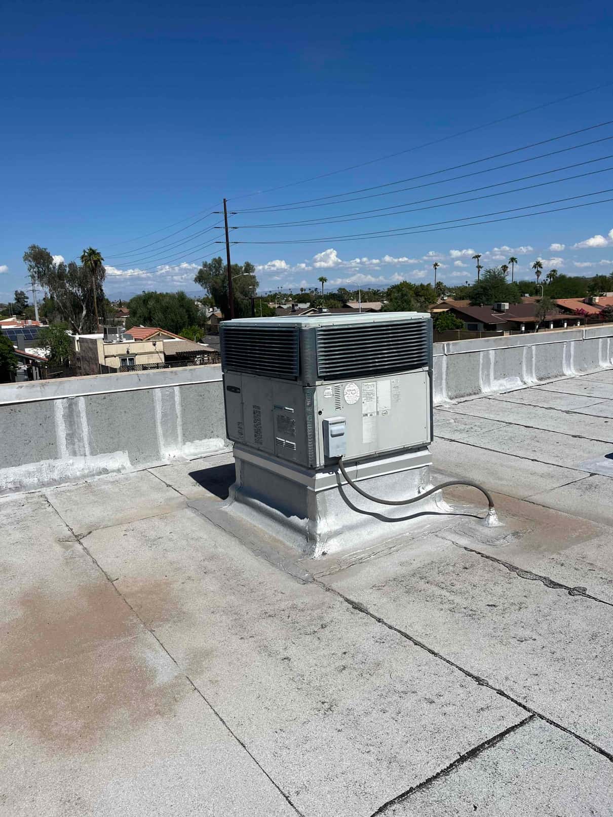 Rooftop packaged HVAC unit on a curb, showing condenser section, access panels, and flexible electrical conduit.