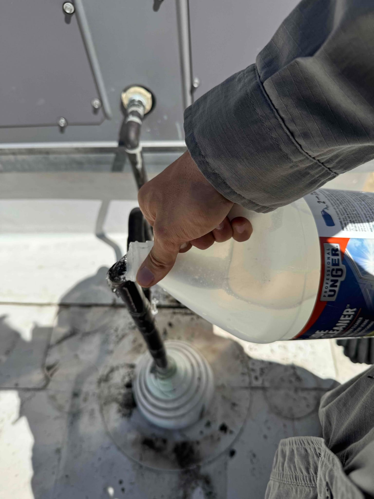 Technician pours cleaning solution into a rooftop condensate drain line with a rubber roof boot during maintenance.