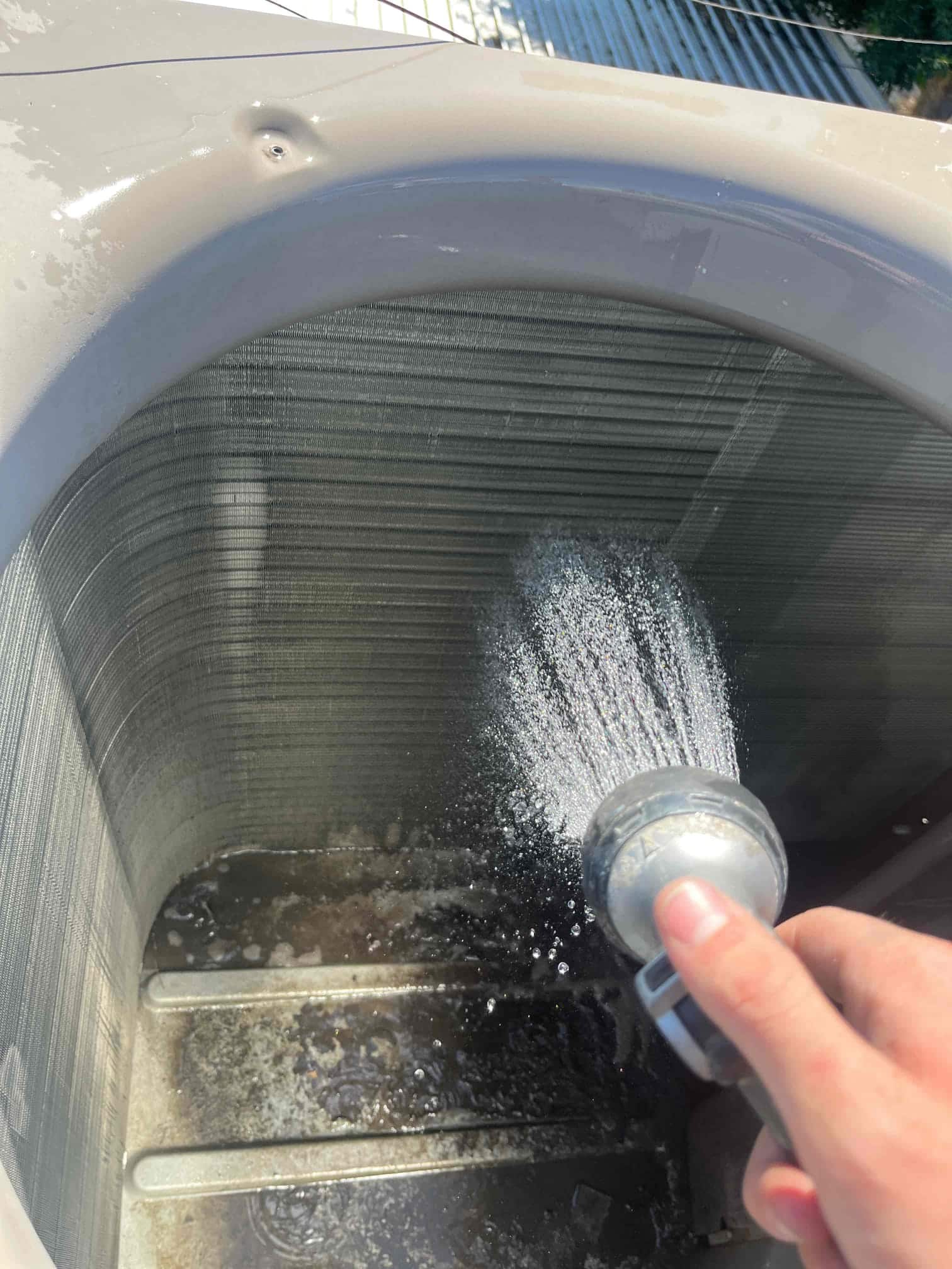 Technician rinses debris from the evaporator-style coil fins inside the outdoor unit housing during cleaning and maintenance.