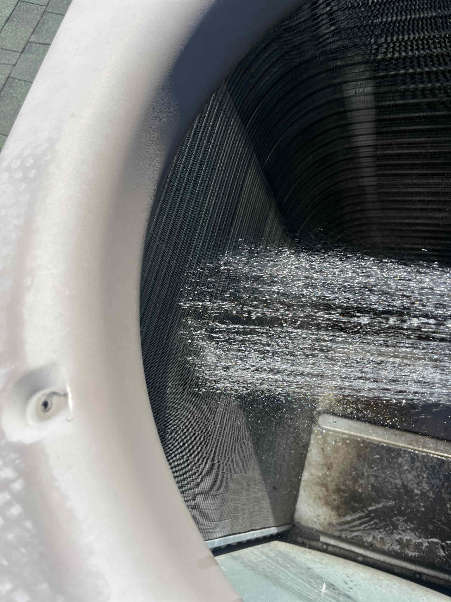 Technician rinses the outdoor condenser coil fins with water, flushing debris from the coil surface for improved airflow.