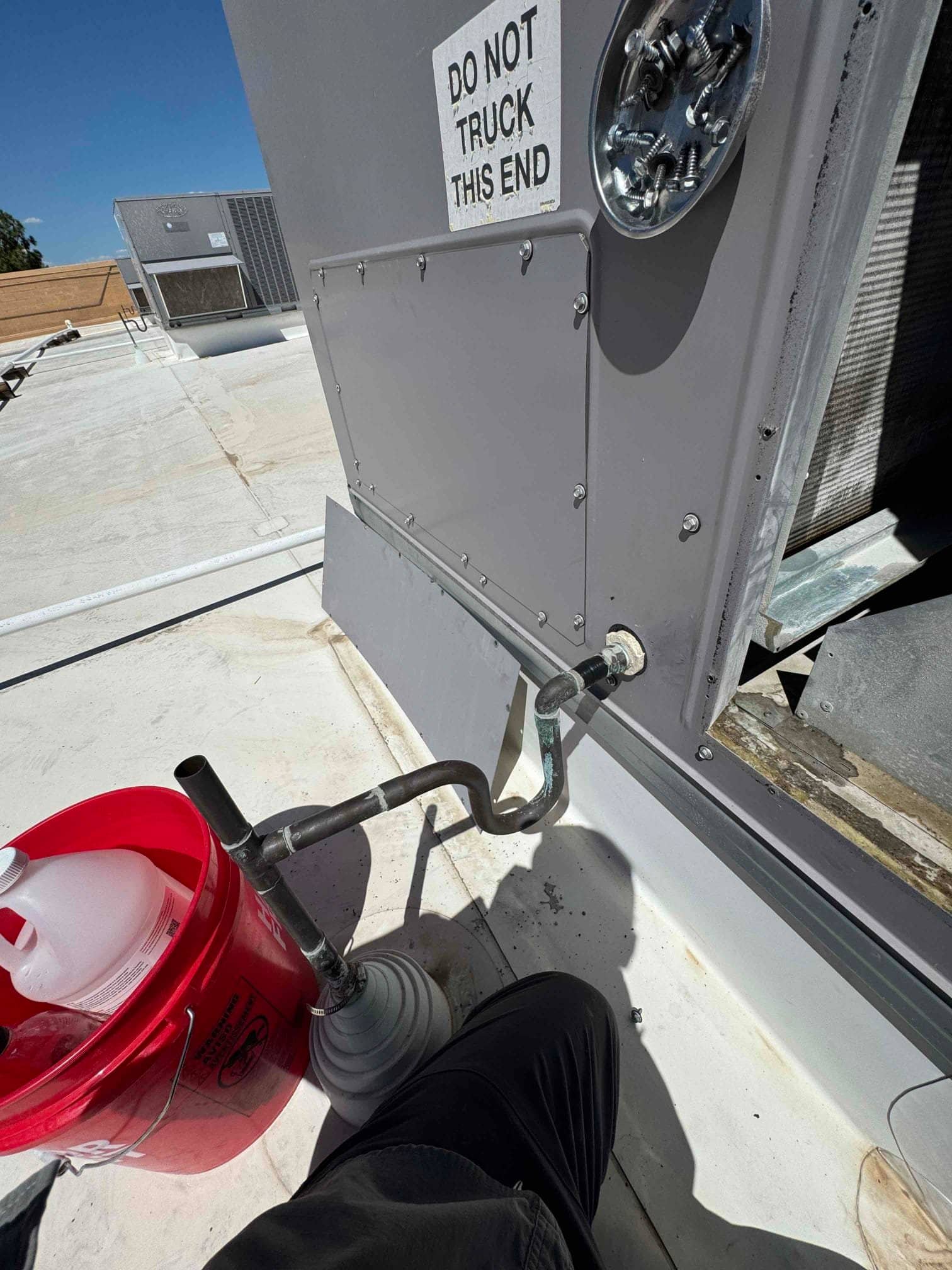 Technician services rooftop air conditioning unit, connecting a vacuum pump to the service port during maintenance.