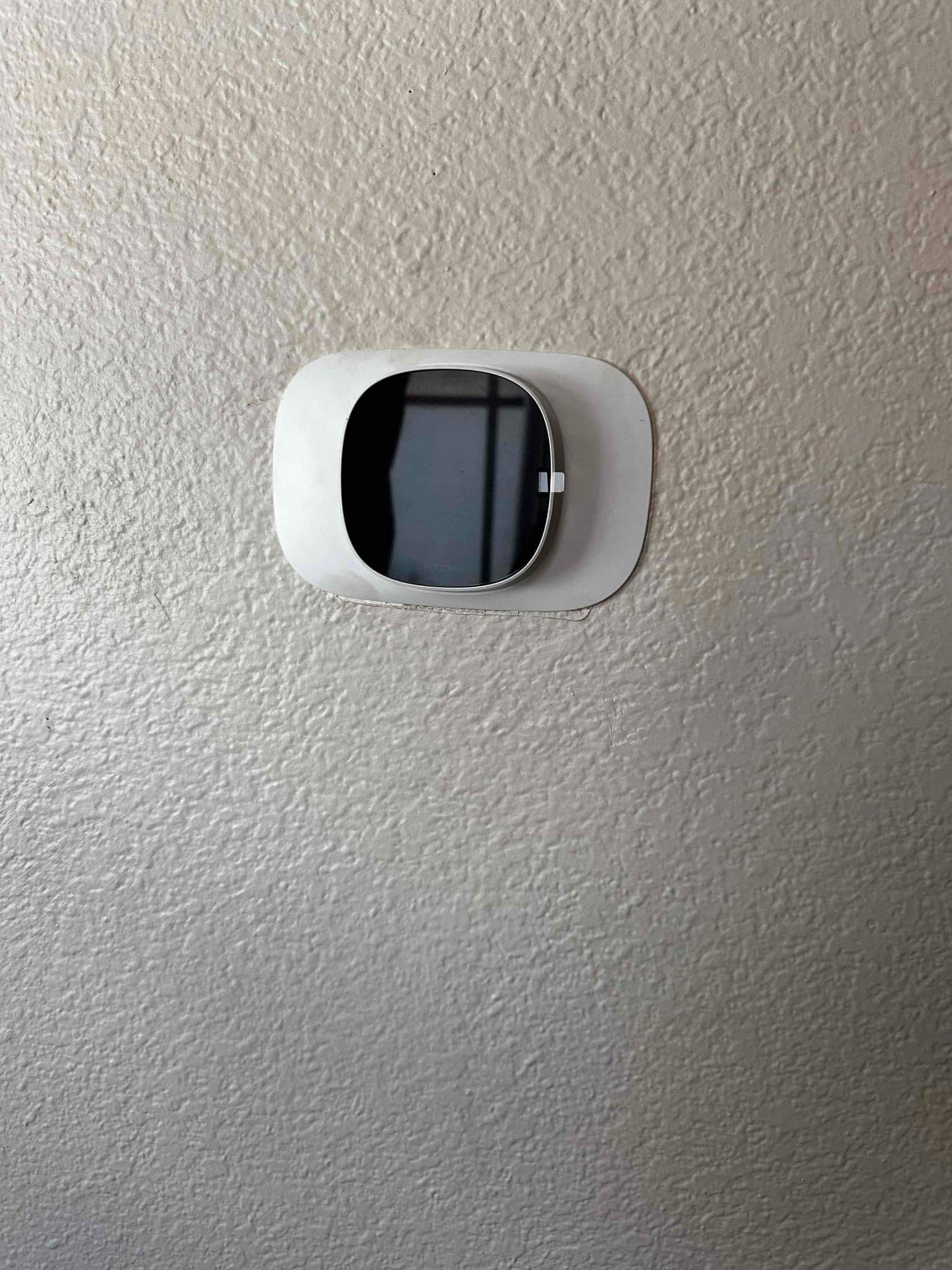 Wall-mounted smart thermostat installed with a trim plate, screen off during final walkthrough of the new system.