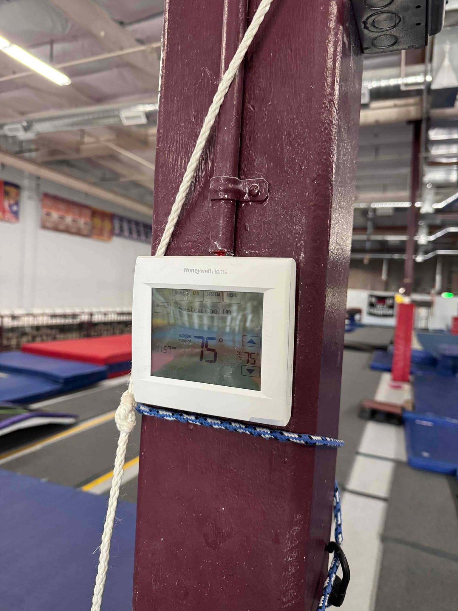 Wall-mounted thermostat displays 75 °F room temperature and 75 °F setpoint in a commercial indoor space.