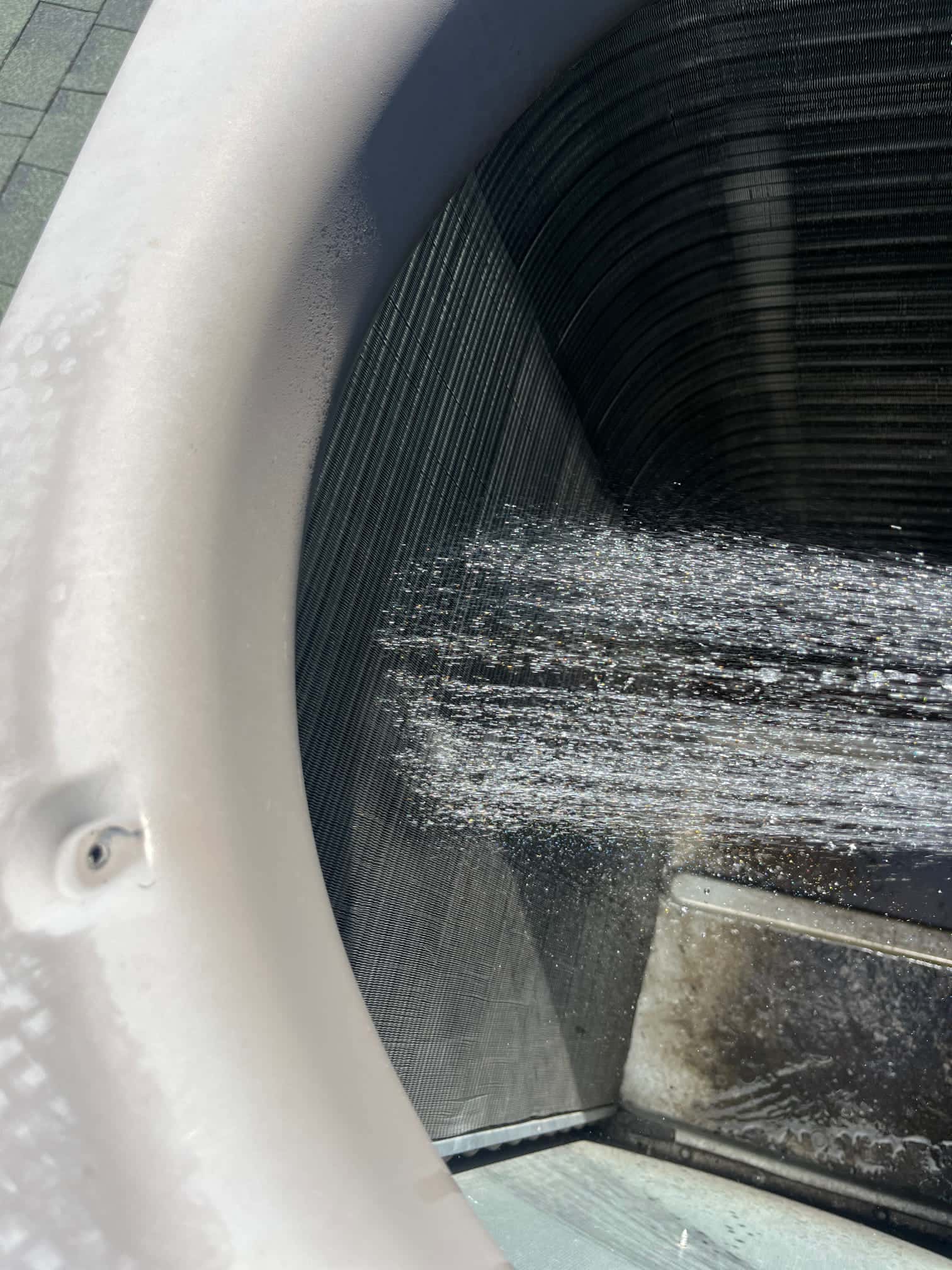 Water spray rinses debris from the outdoor condenser coil fins, showing active evaporator coil cleaning during maintenance.