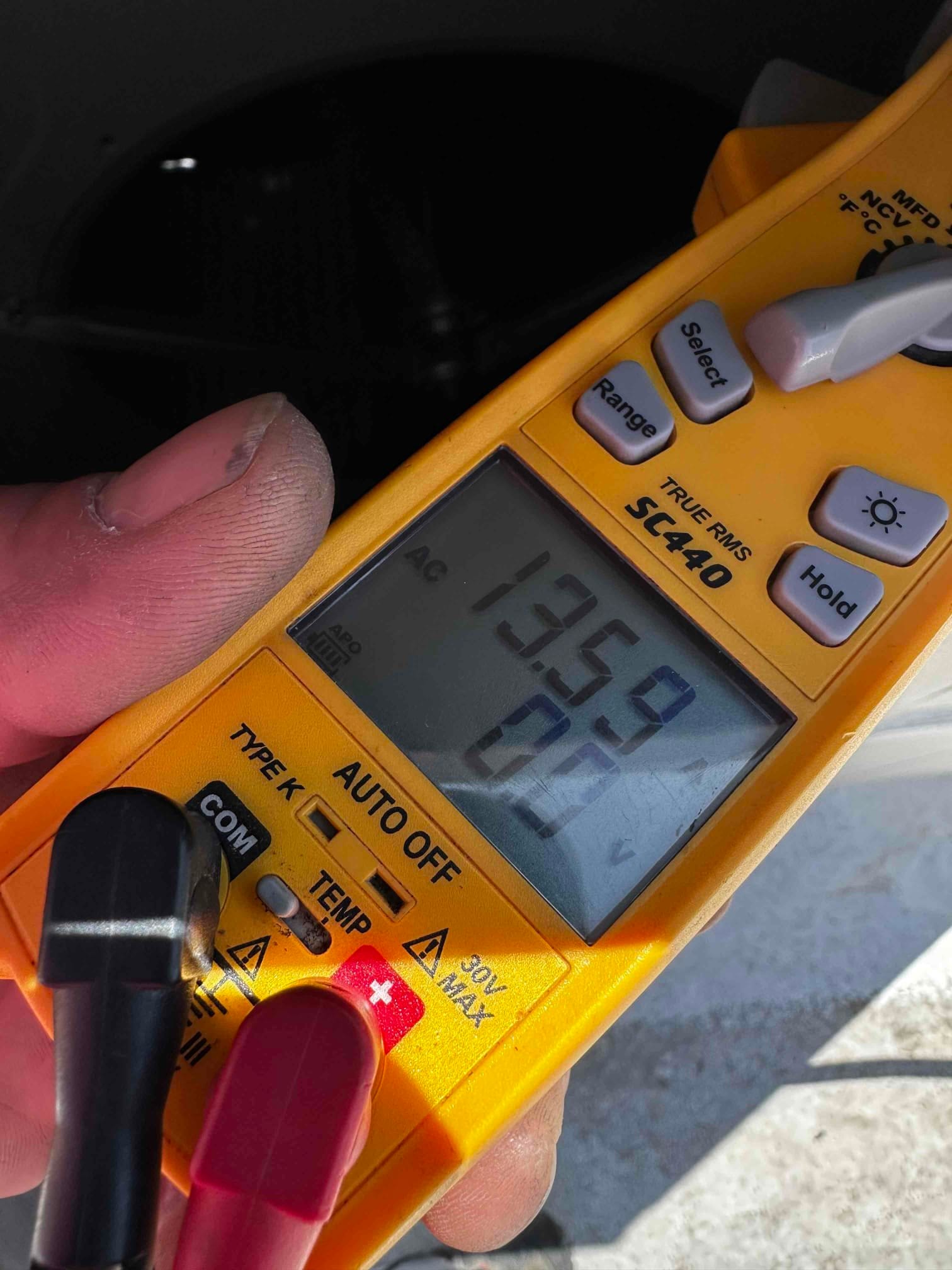 Digital multimeter shows AC voltage measurement with test leads connected, documenting line voltage during HVAC electrical checks.
