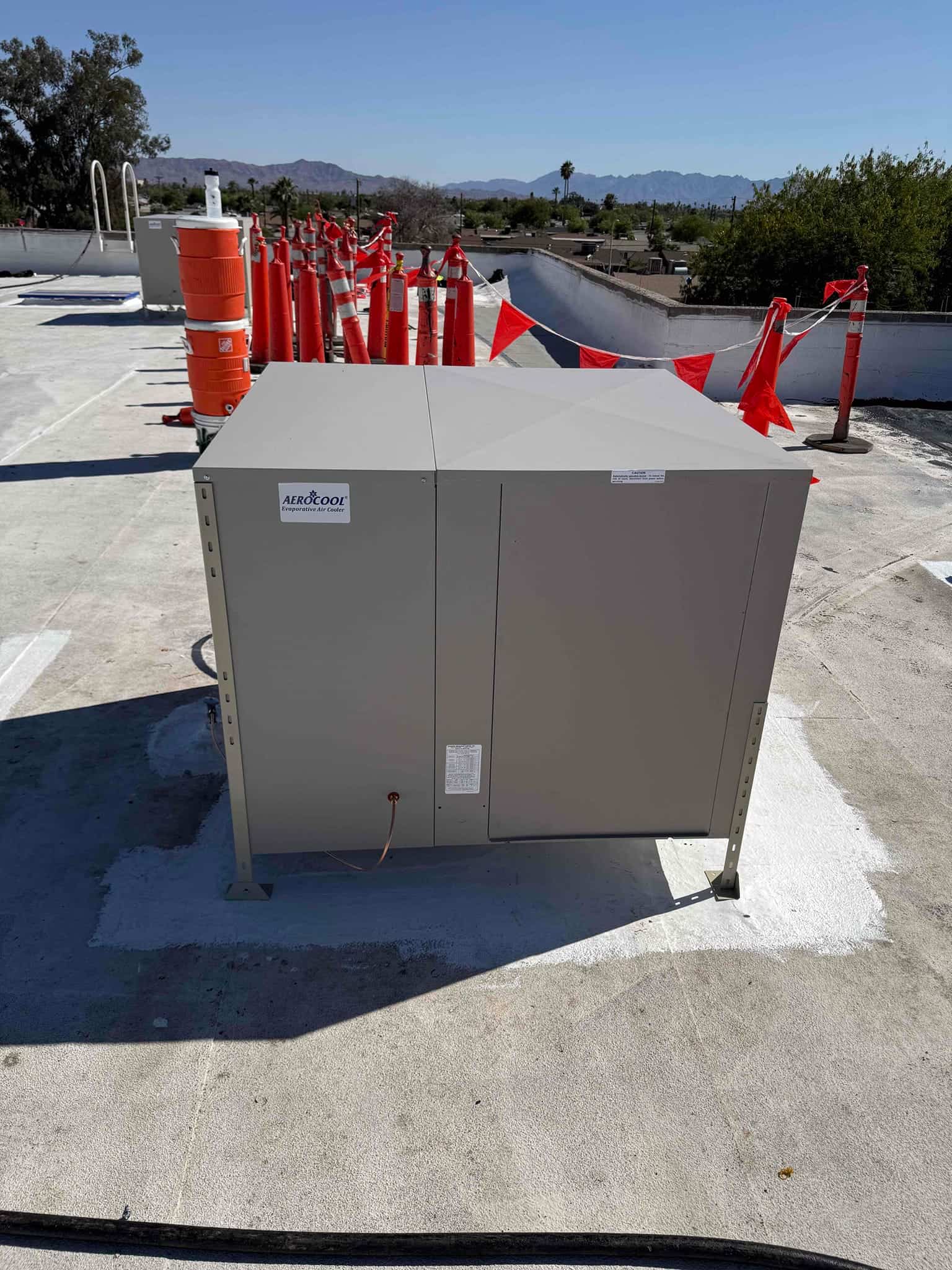 Evaporative cooler installed on rooftop, secured on leveling legs with sealed roof penetrations and safety cones nearby.