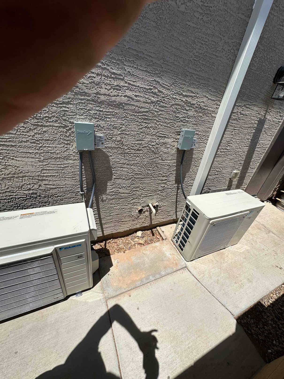 Two mini-split outdoor units installed on concrete pads with weatherproof disconnects and line set covers along the exterior wall.