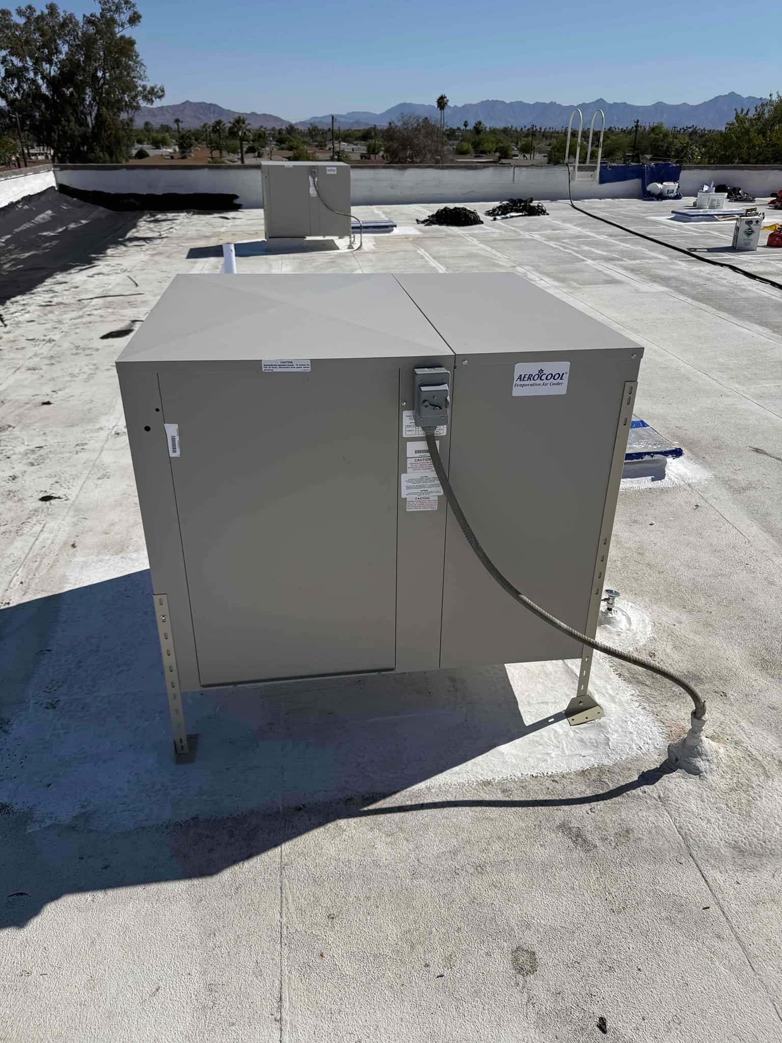 New rooftop evaporative cooler installed on raised stands with electrical whip connected and roof penetration sealed.