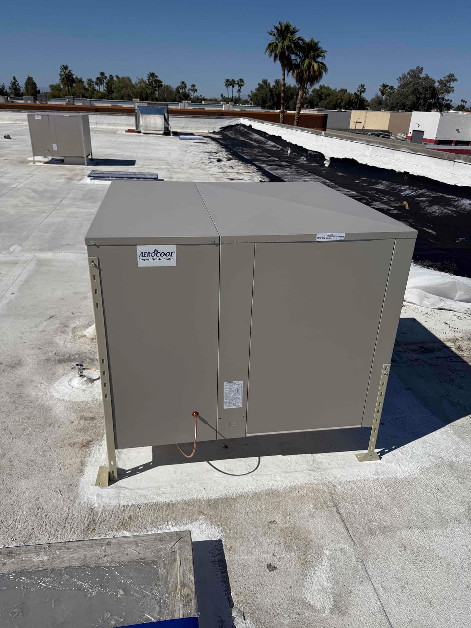 New rooftop evaporative cooler mounted on elevated stands with sealed roof curb and surrounding rooftop equipment visible.