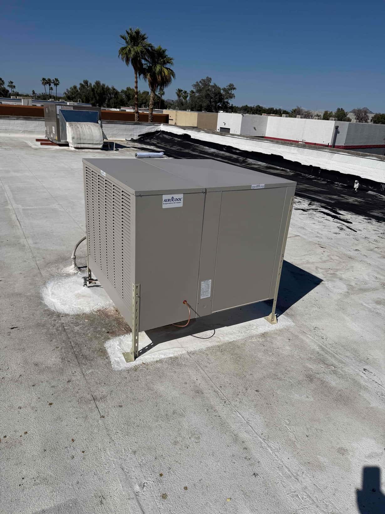 New rooftop evaporative cooler set and secured on curbs with roof penetrations sealed and adjacent ductwork visible.