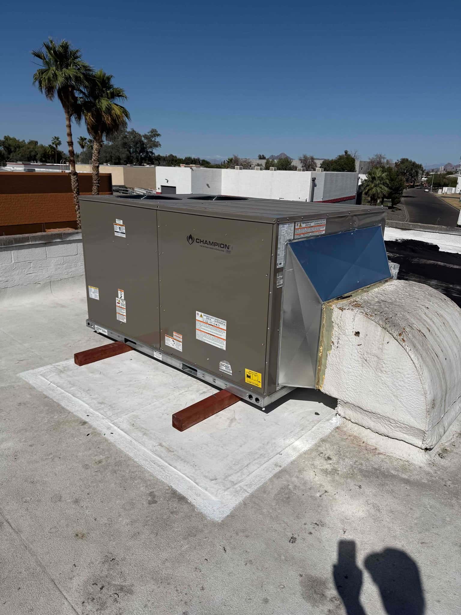 New rooftop packaged HVAC unit set on curb with sealed supply duct connection and protective support rails on the roof.