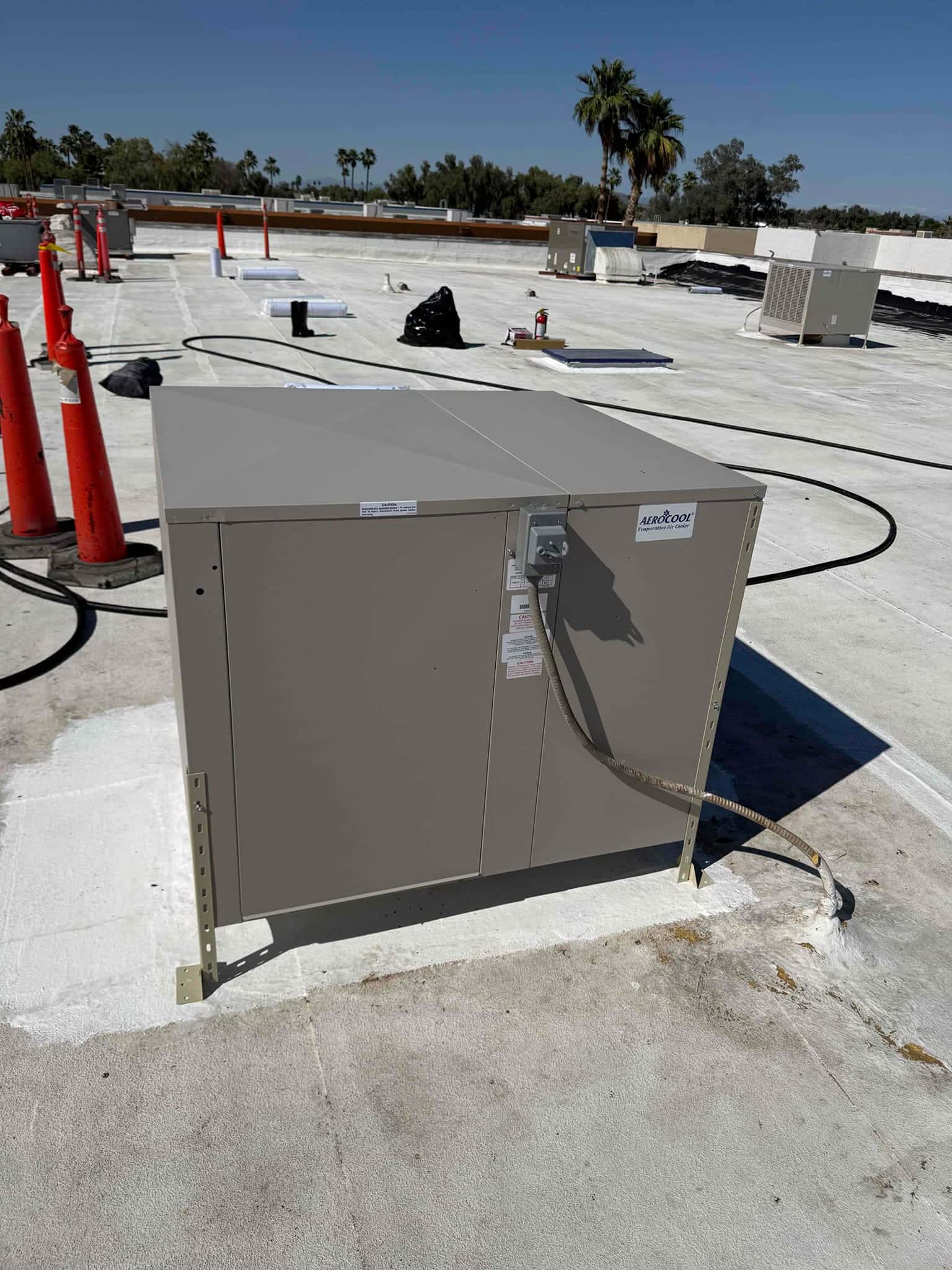 New rooftop unit set on a sealed curb with electrical whip connected, surrounded by cones and installation materials.