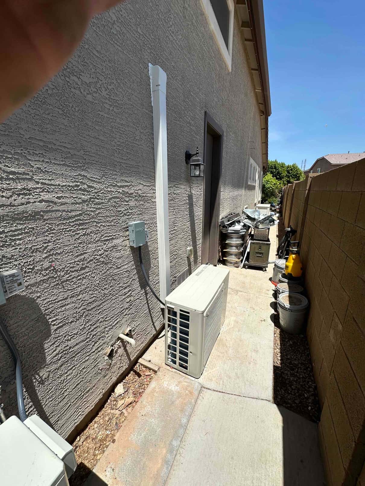 Outdoor mini-split condenser set on a walkway beside the house with line-set cover and electrical disconnect installed.