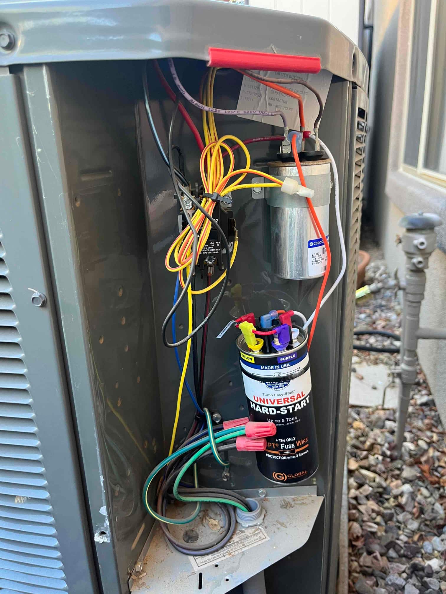 Condenser electrical compartment open, showing contactor, run capacitor, and installed universal hard-start kit with connected wiring.